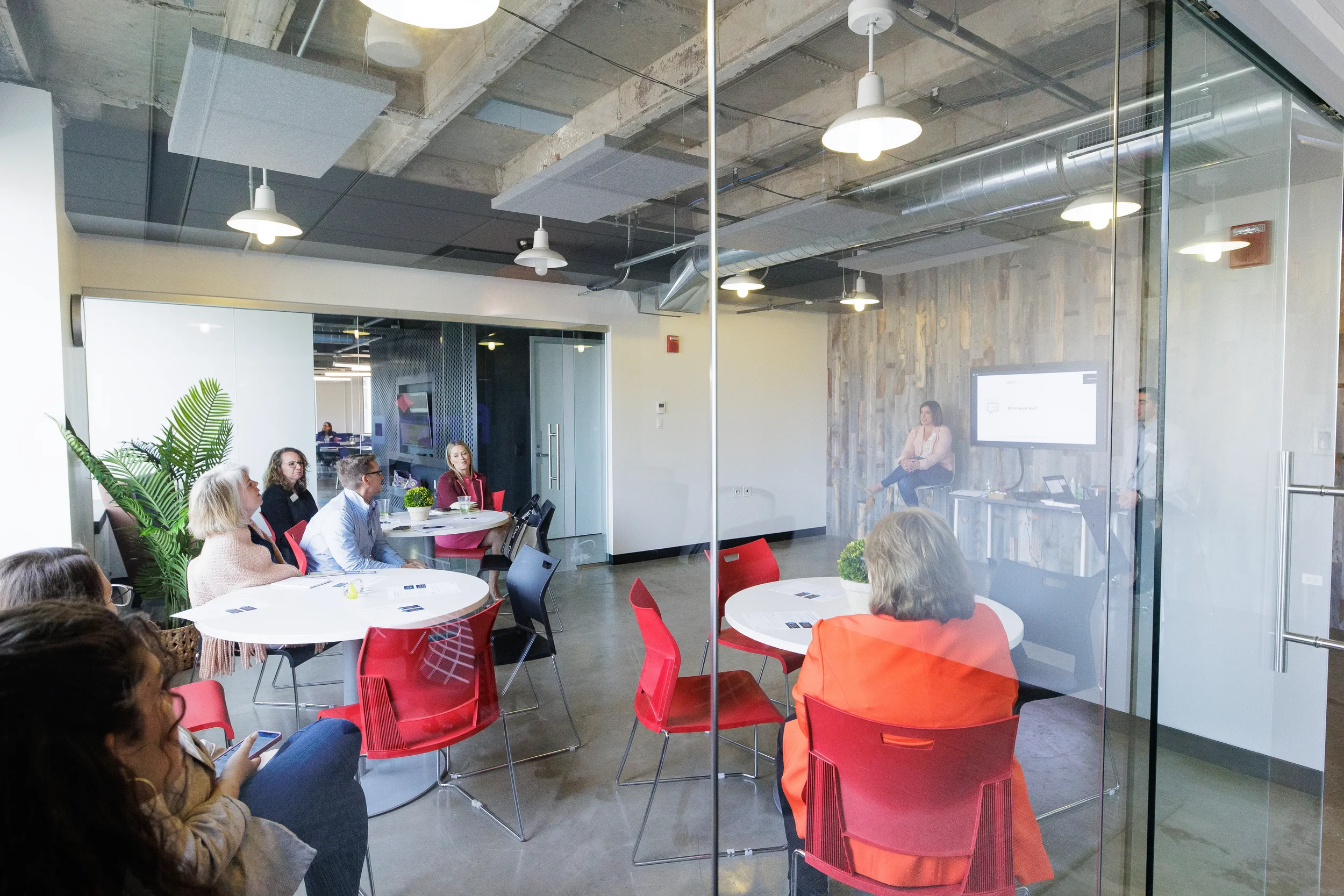 Wide view through glass wall of attendees seated at round tables during Chicago conference breakout session