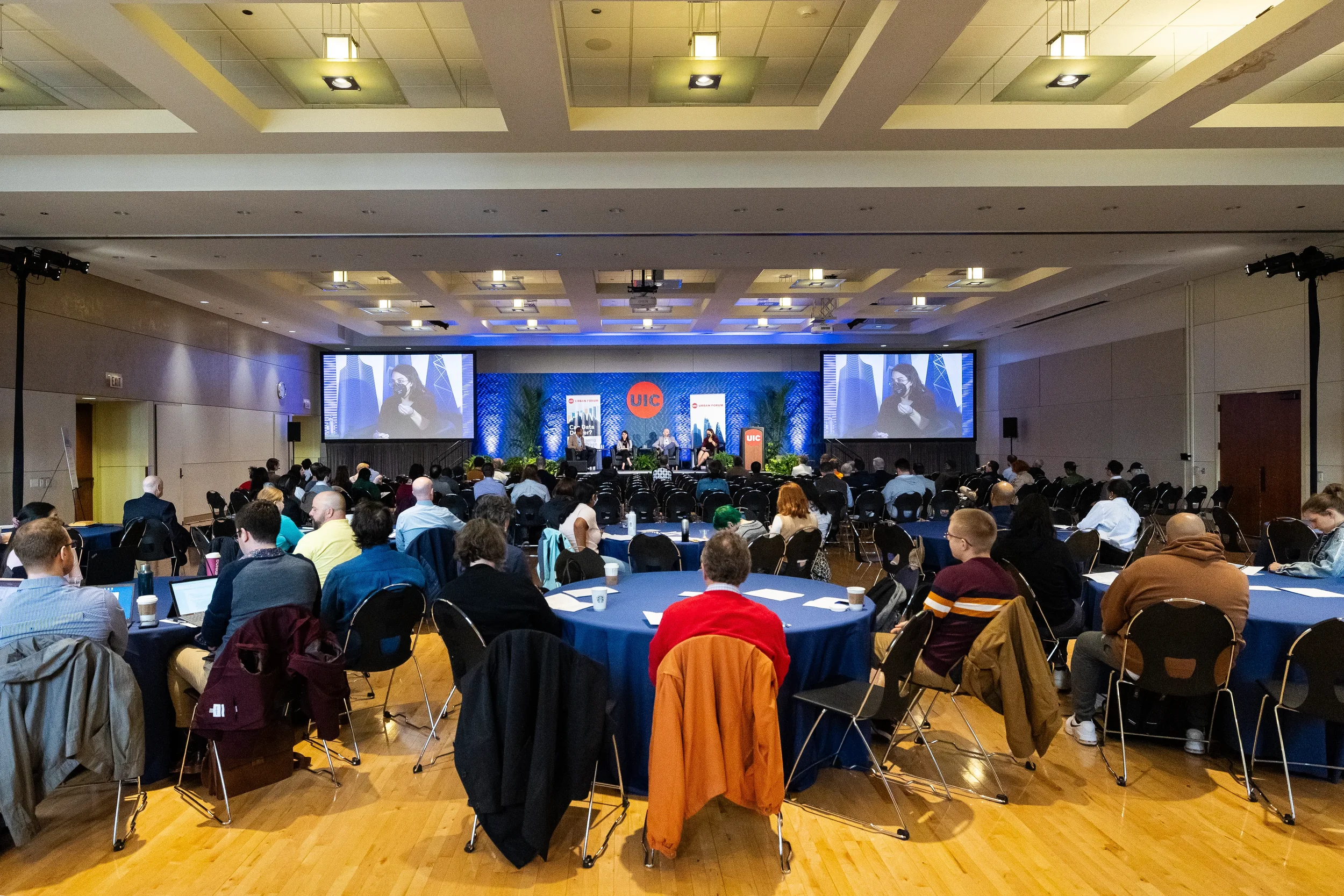 Wide ballroom view of audience at roundtables watching panel on screens at Chicago conference