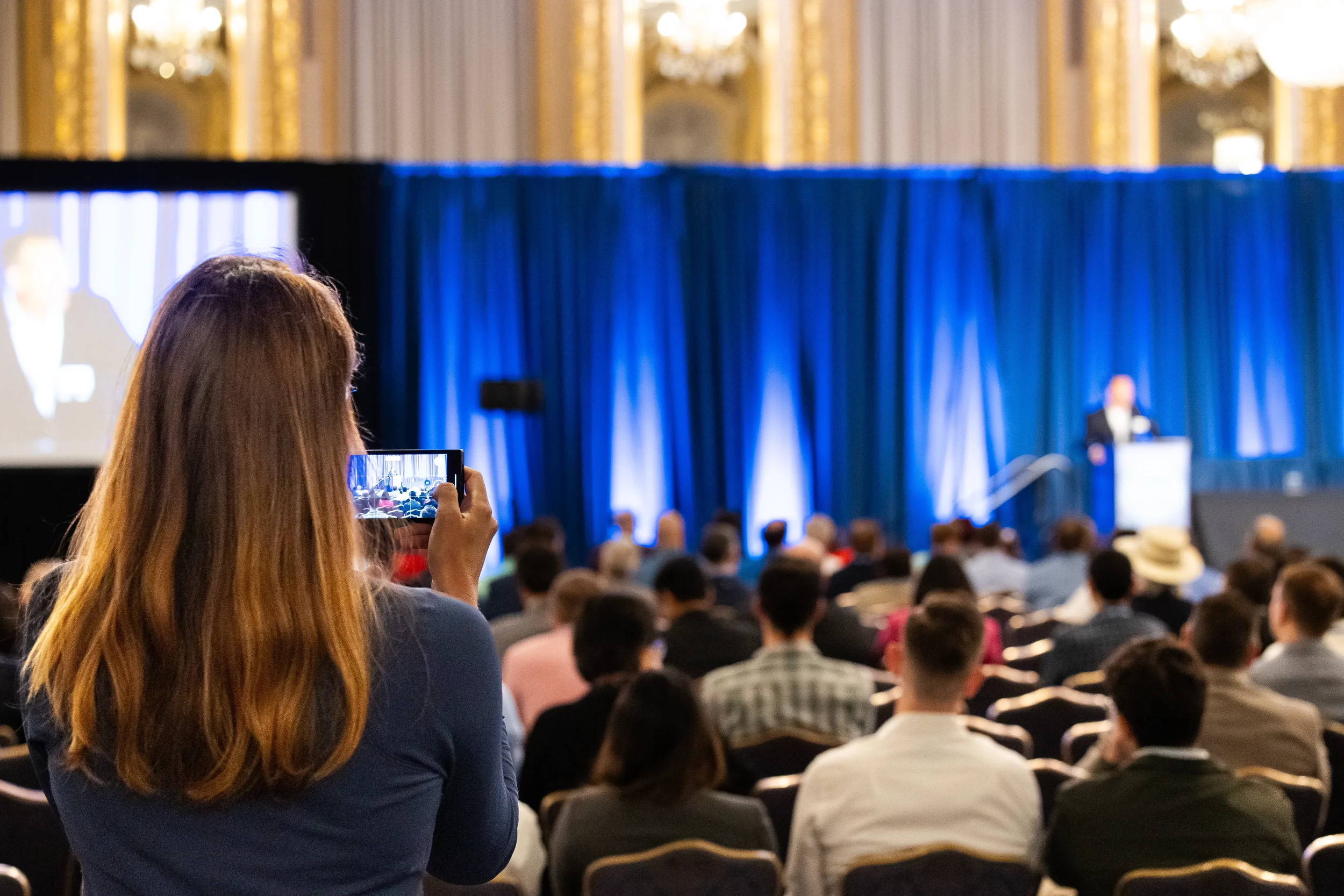 Attendee records keynote presentation on smartphone during AACE International session in Chicago