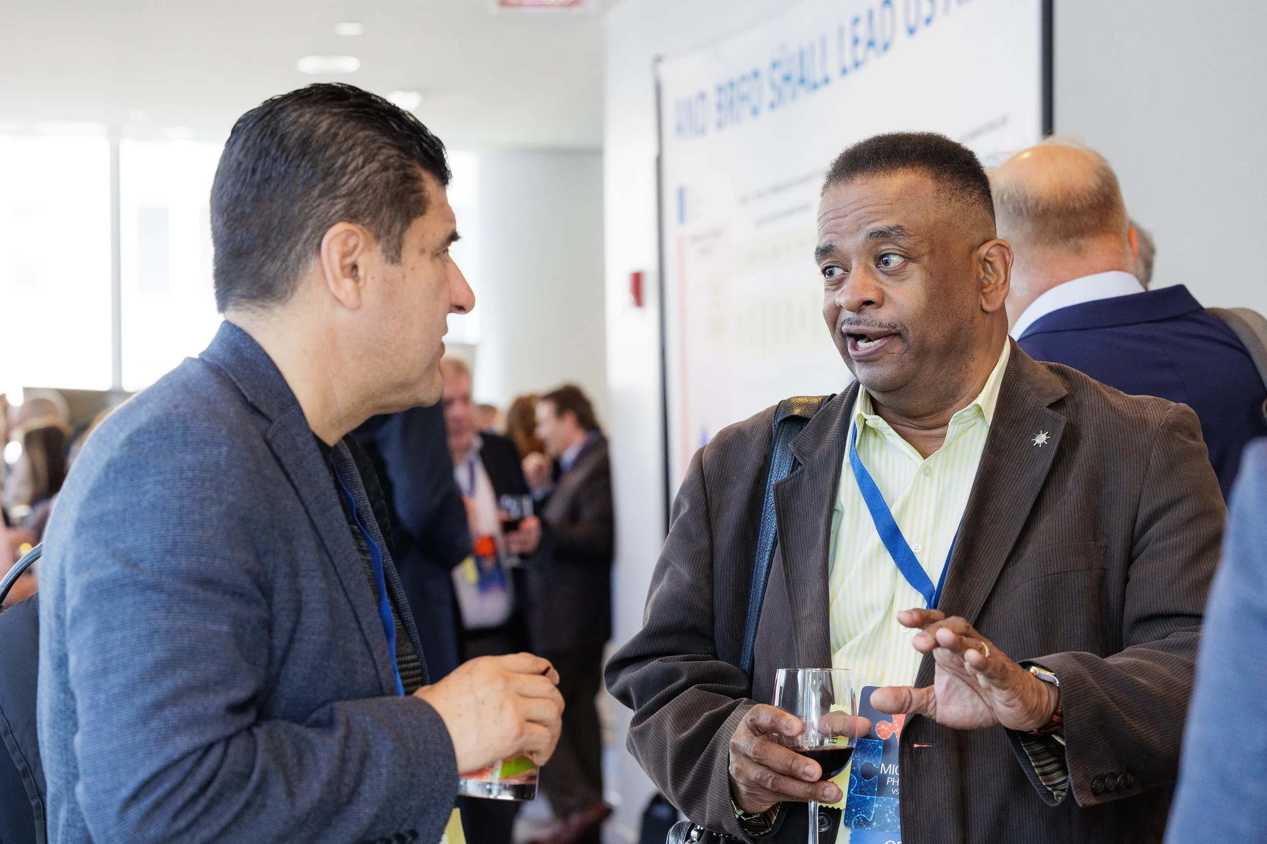 Two male attendees with lanyards converse animatedly over drinks at Orlando industry conference networking