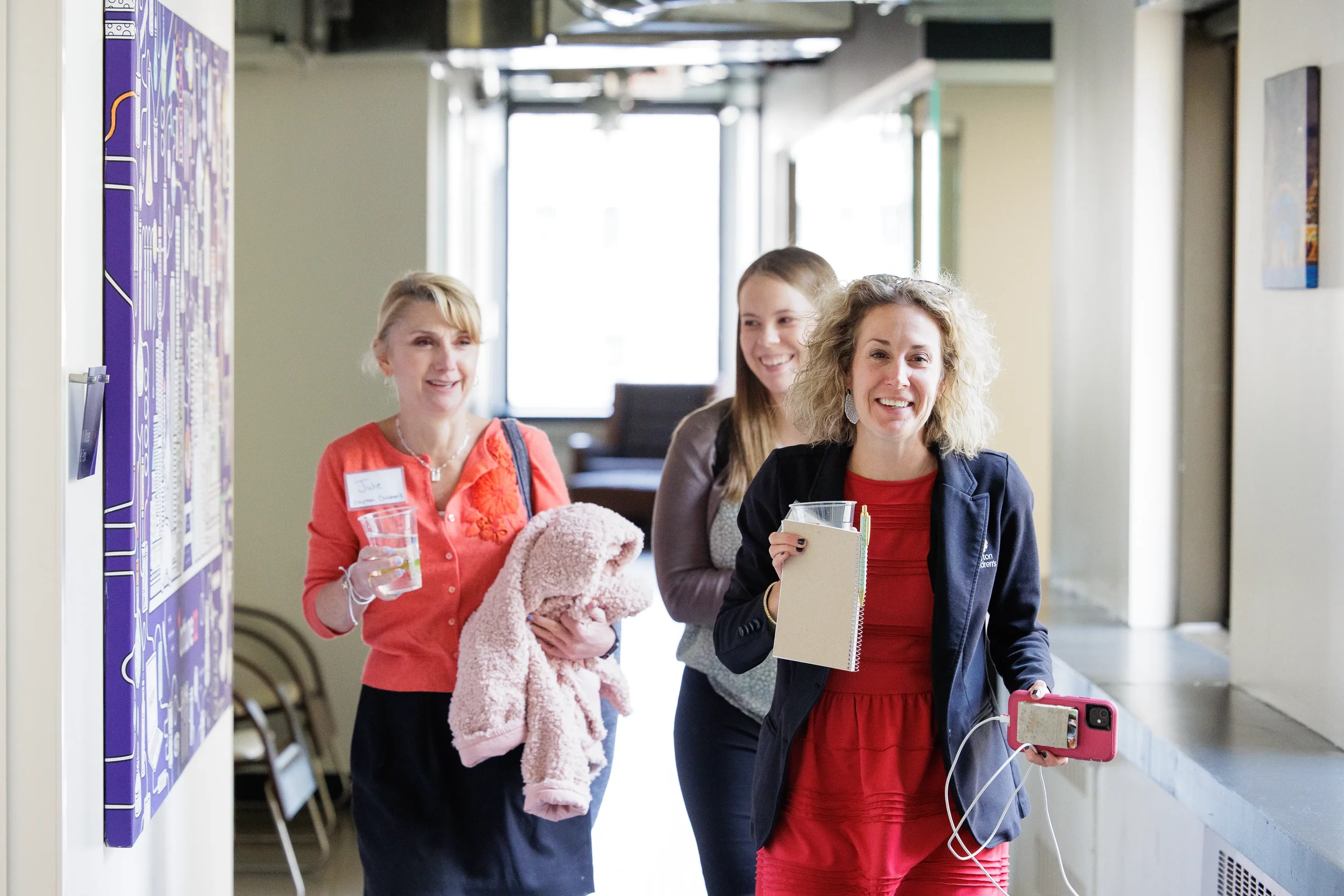 Three smiling female attendees walk through a bright venue hallway at Orlando corporate conference