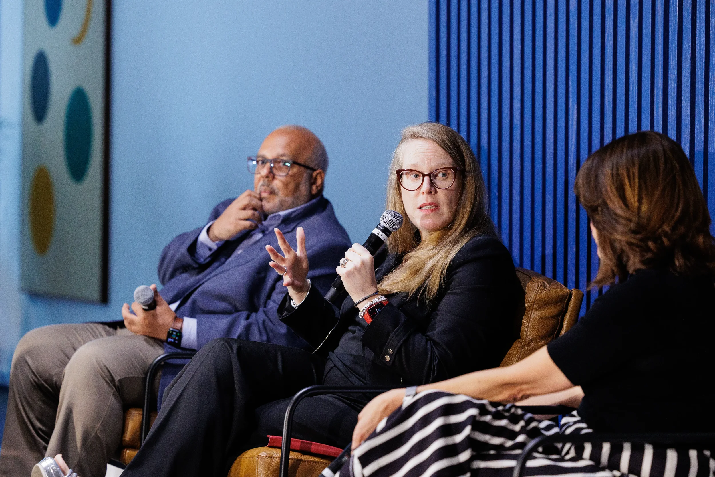 Panelist speaks into microphone with hand raised while fellow speakers listen on stage at Chicago corporate conference