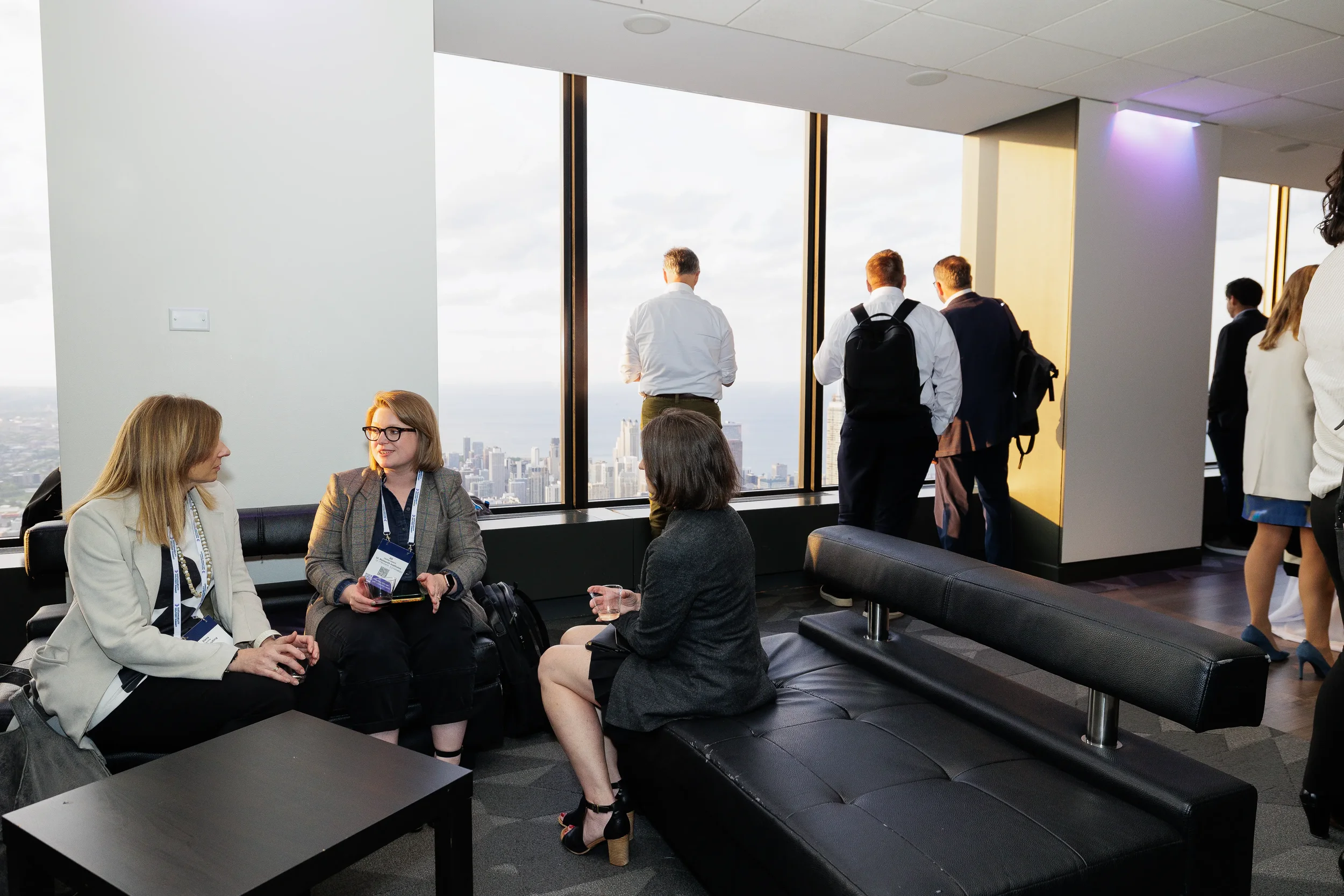 Attendees converse in lounge seating with Chicago skyline view during conference reception