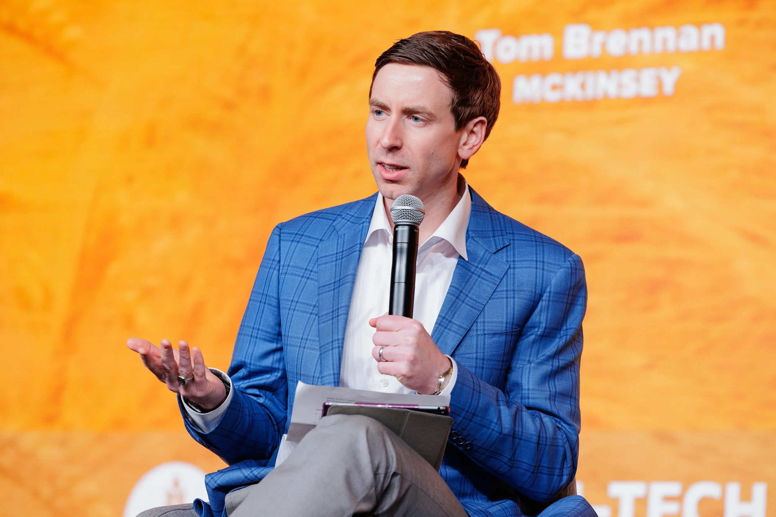 Speaker in blue blazer presents with microphone and notes on stage at Chicago industry summit