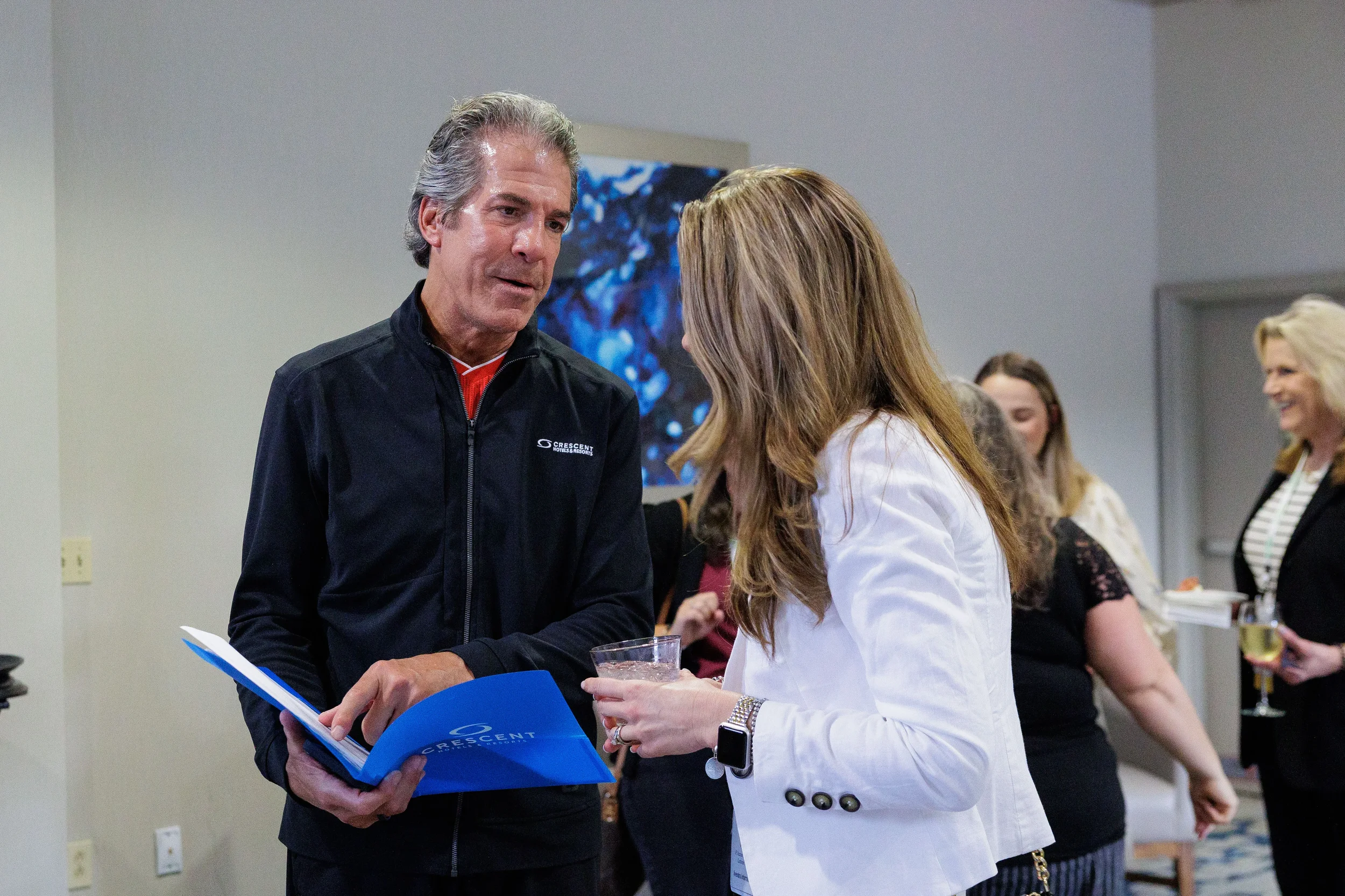 Two attendees converse during networking reception with branded folder at Orlando corporate conference