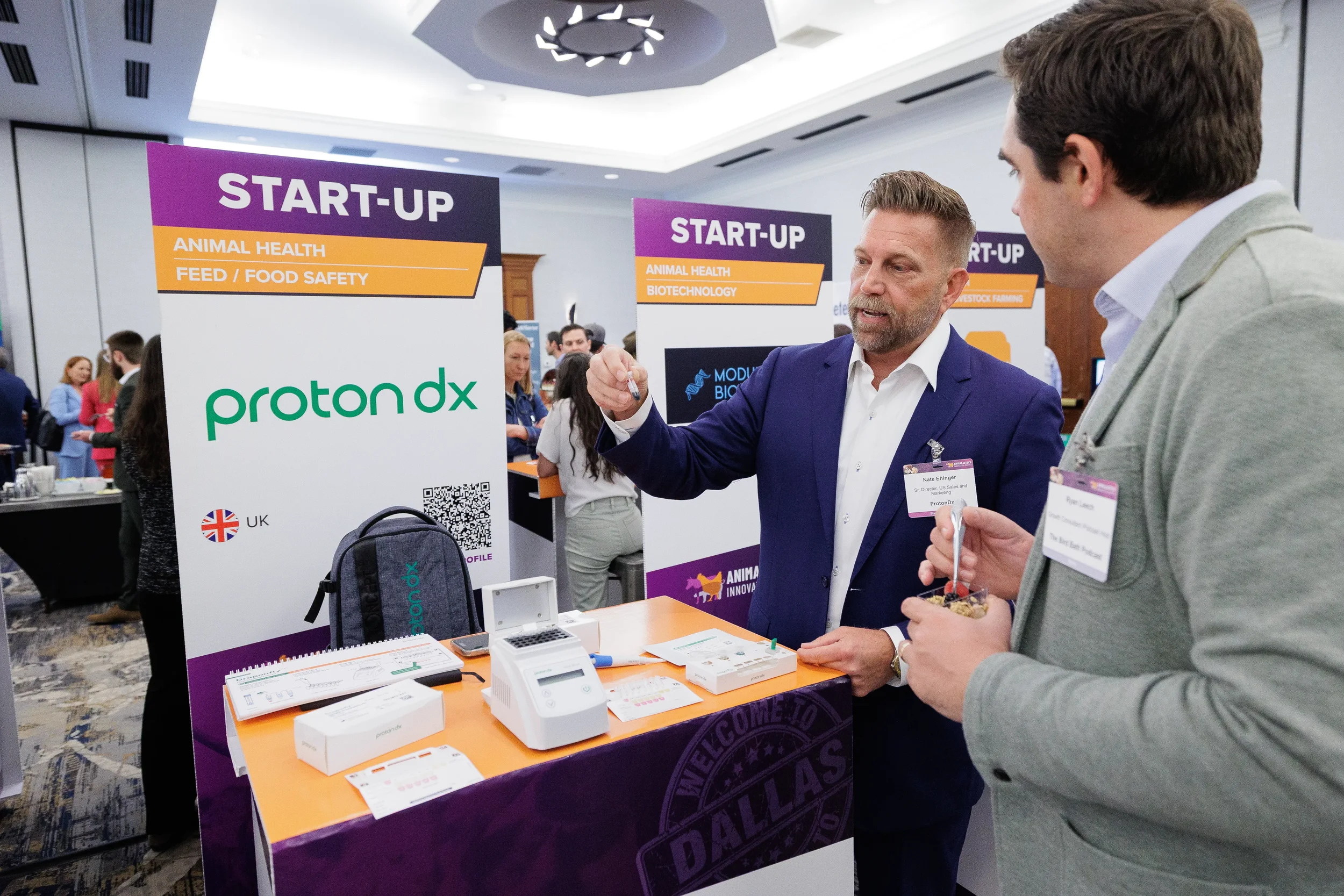 Attendee demonstrates product to visitor at startup booth during Orlando industry trade show