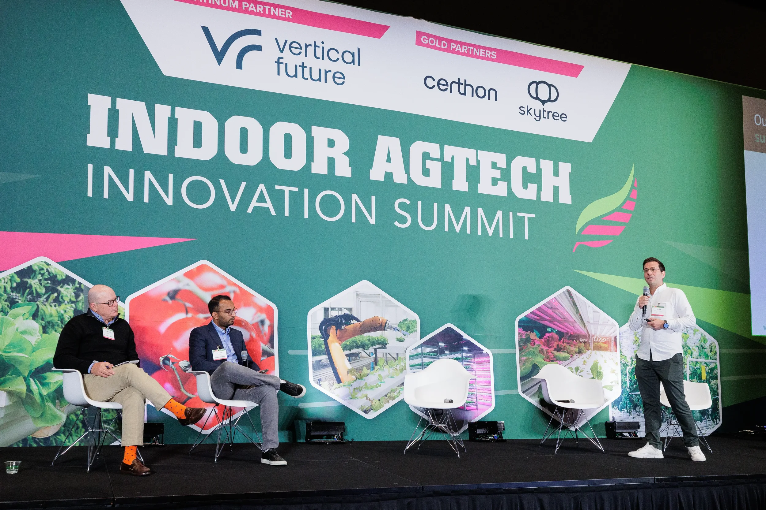 Panelist stands with microphone while fellow speakers listen on stage in front of branded backdrop at Chicago industry conference