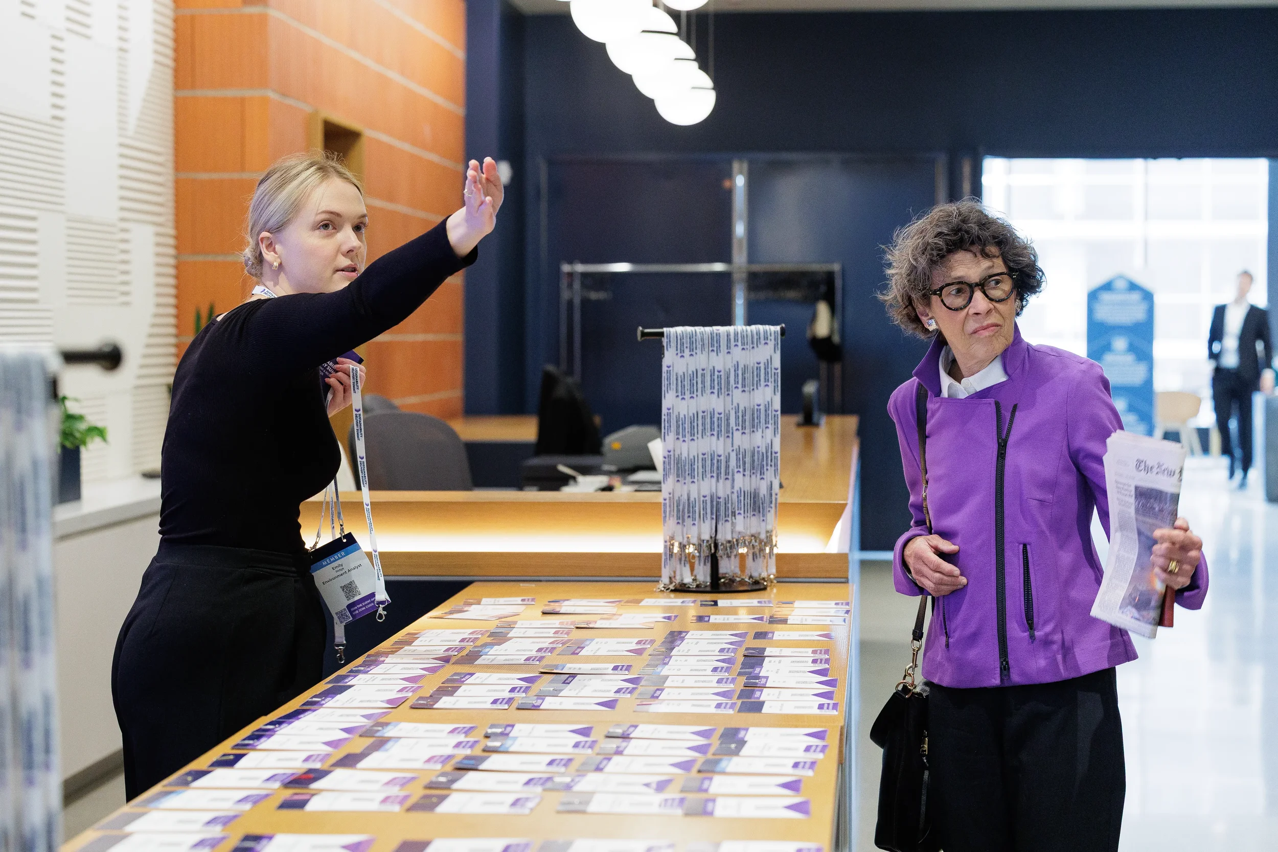 Attendee points toward badge display while assisting guest at Orlando conference registration table