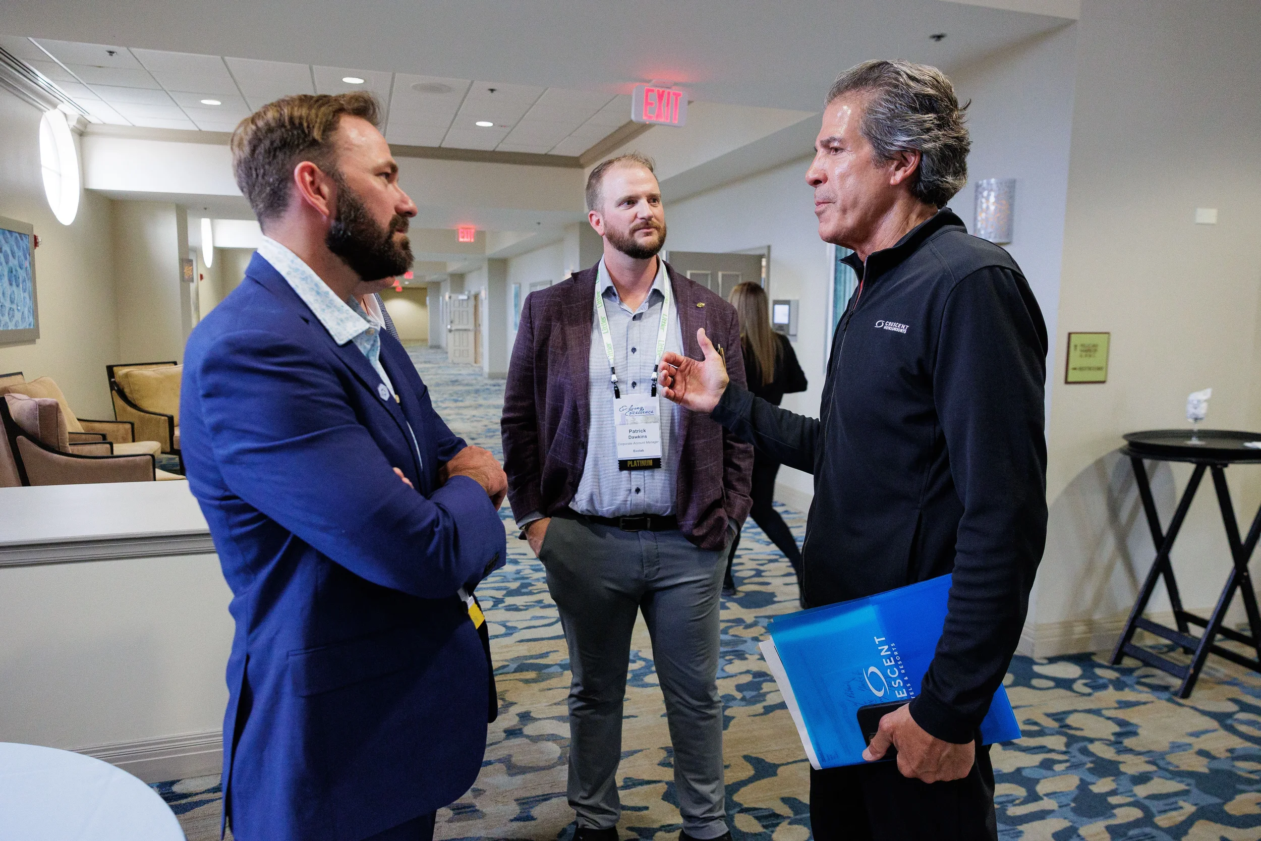 Three male attendees with lanyards converse in hotel hallway during Chicago corporate conference