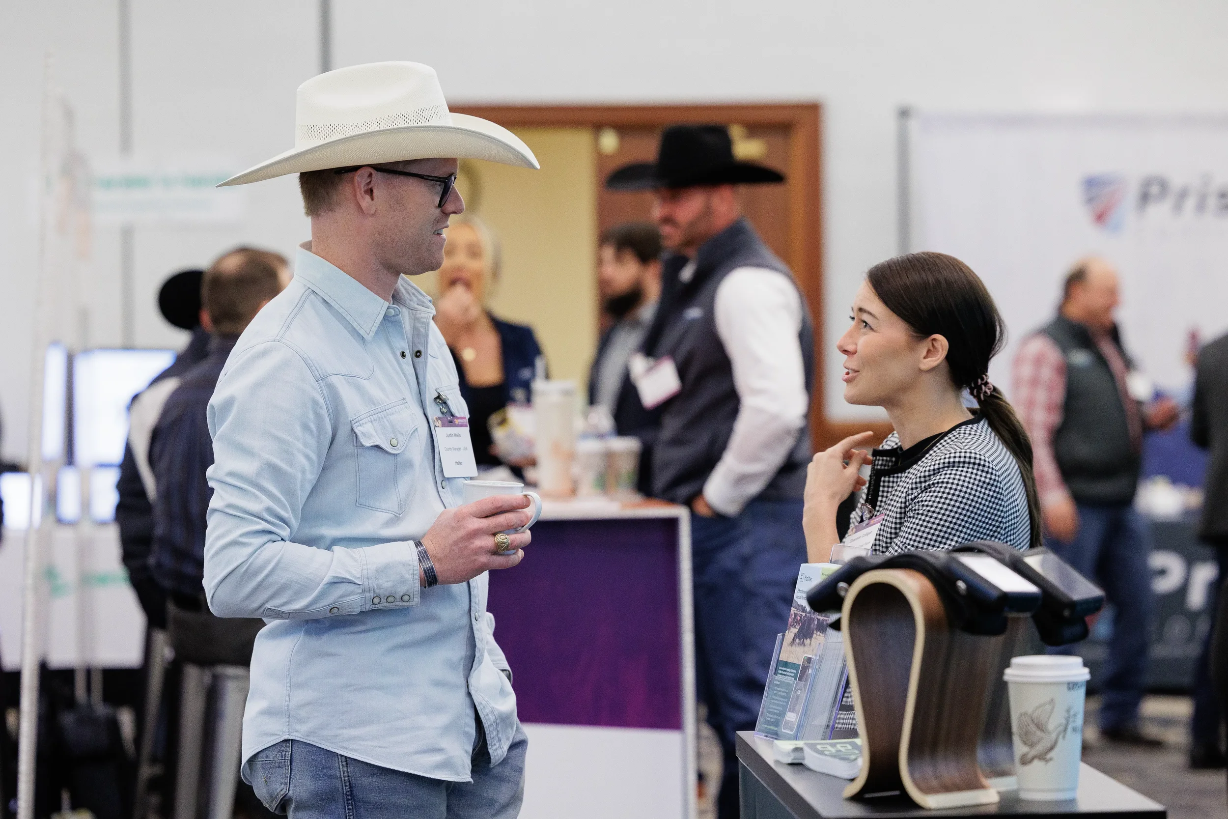 Attendee wearing cowboy hat holds coffee while conversing at expo booth in Chicago