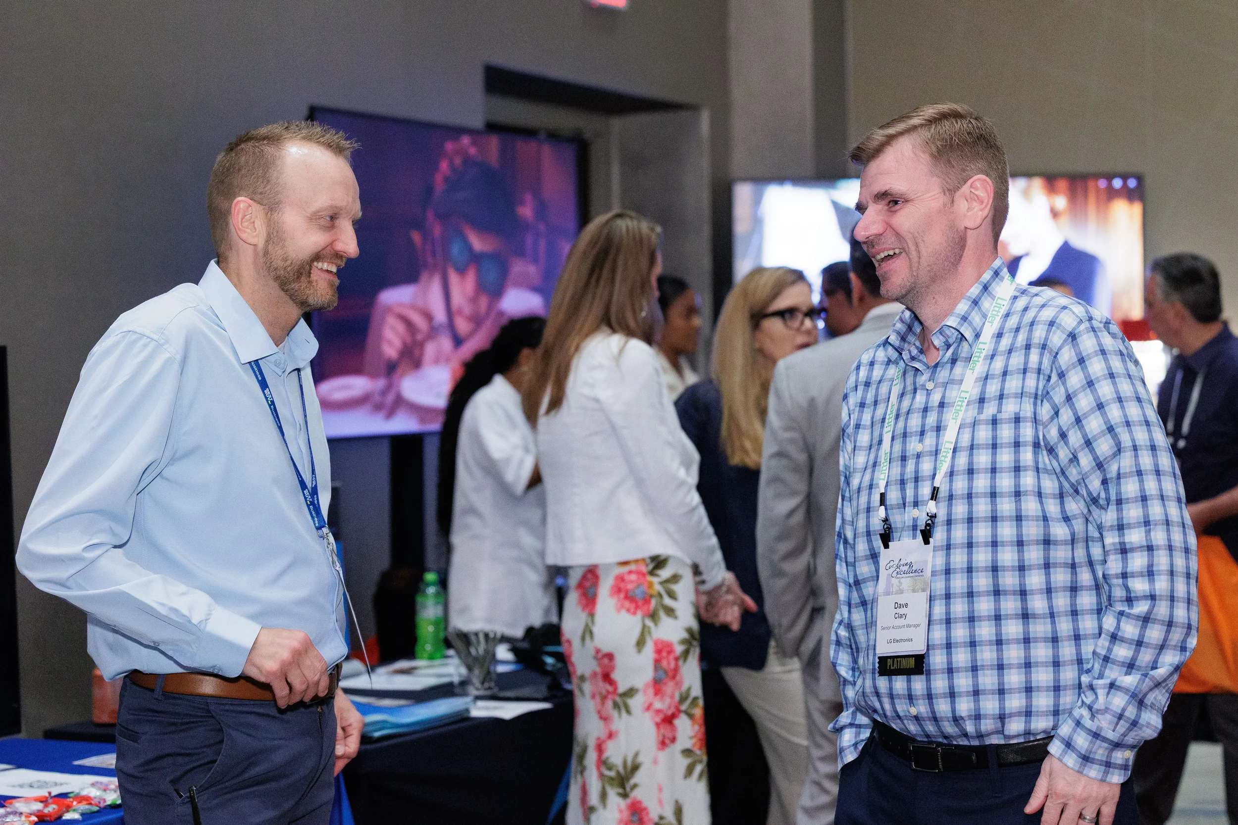 Two male attendees with lanyards laugh together on expo floor at Orlando industry conference