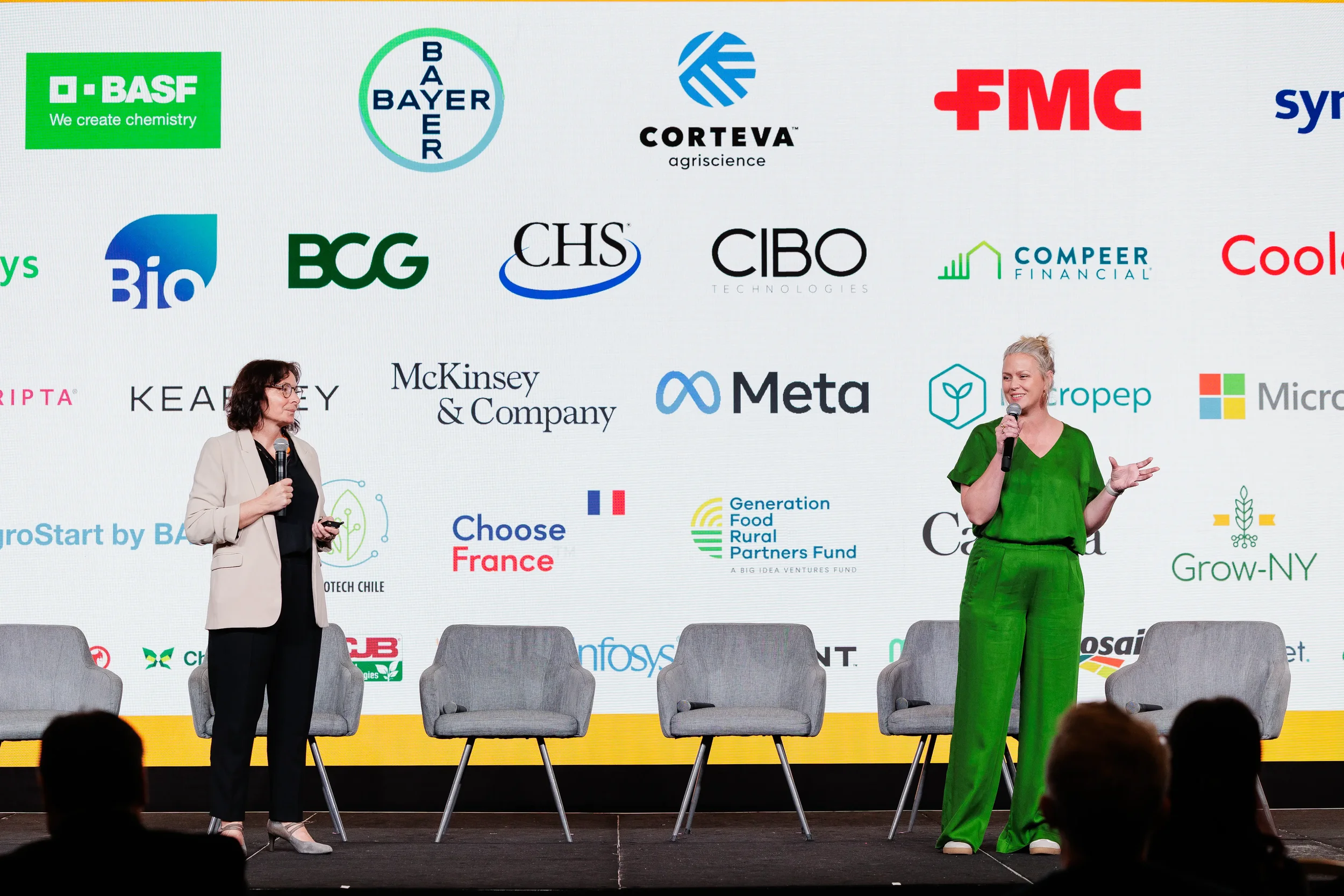 Two speakers with microphones on stage in front of multi-sponsor backdrop at Orlando corporate event