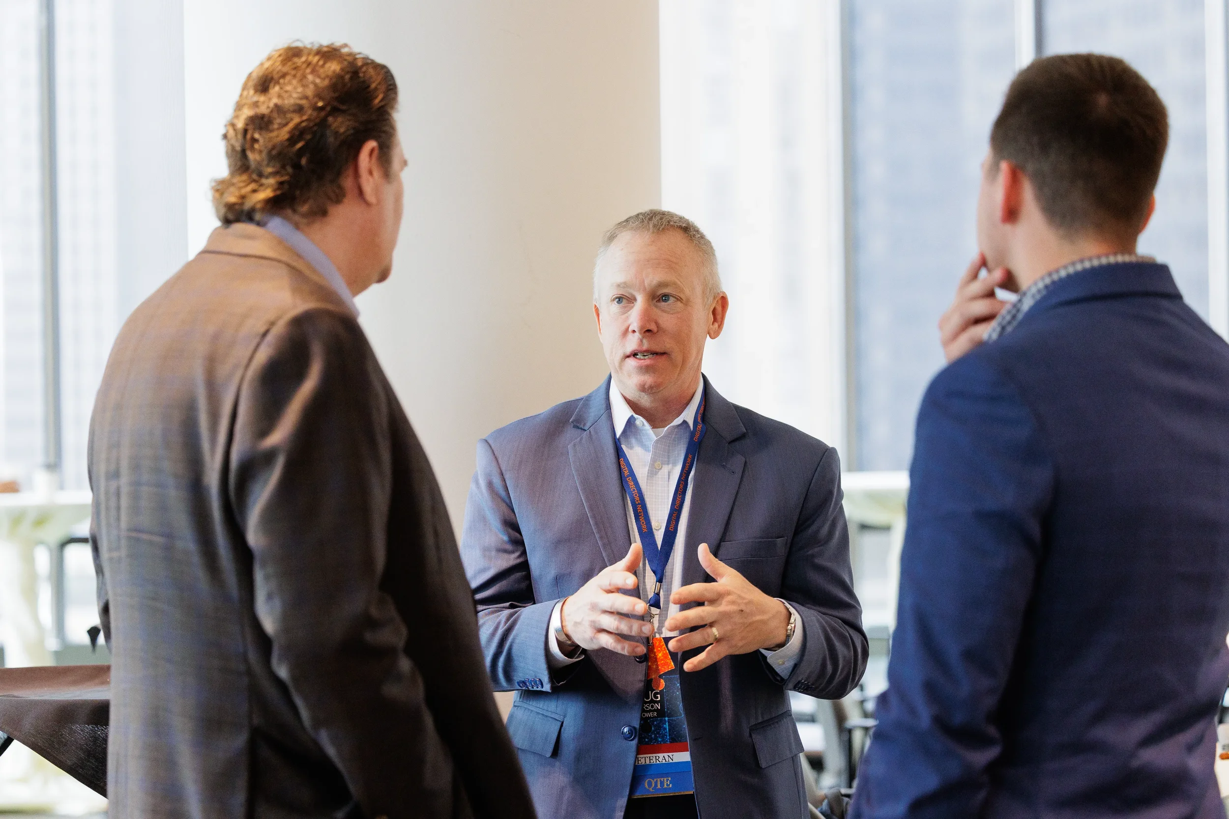 Three male attendees with lanyards converse in small group during Orlando corporate conference networking