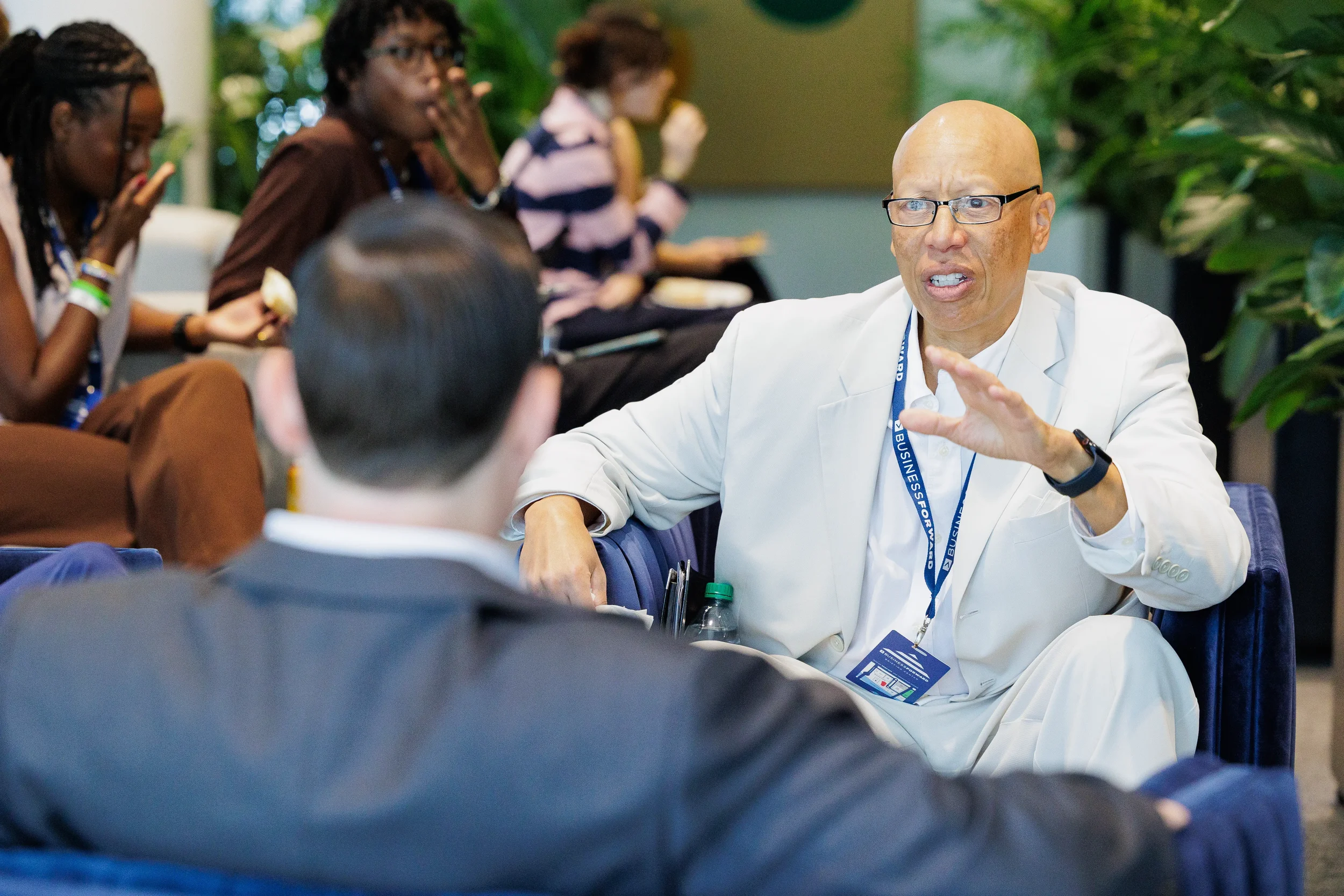 Attendee in white suit gestures expressively while in conversation during networking break at Chicago corporate conference