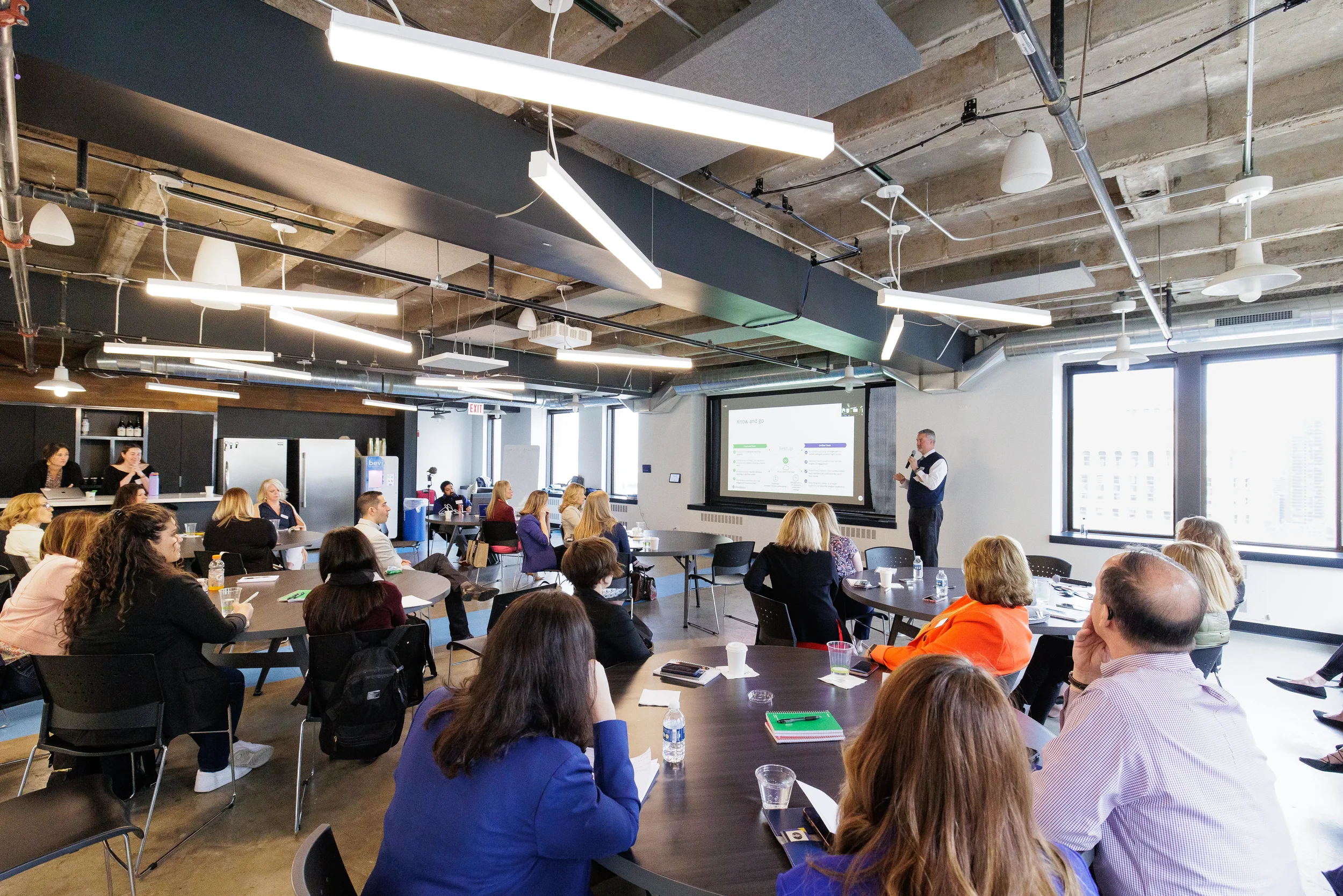 Wide view of a full conference room with a male speaker beside a projection screen at Orlando corporate event