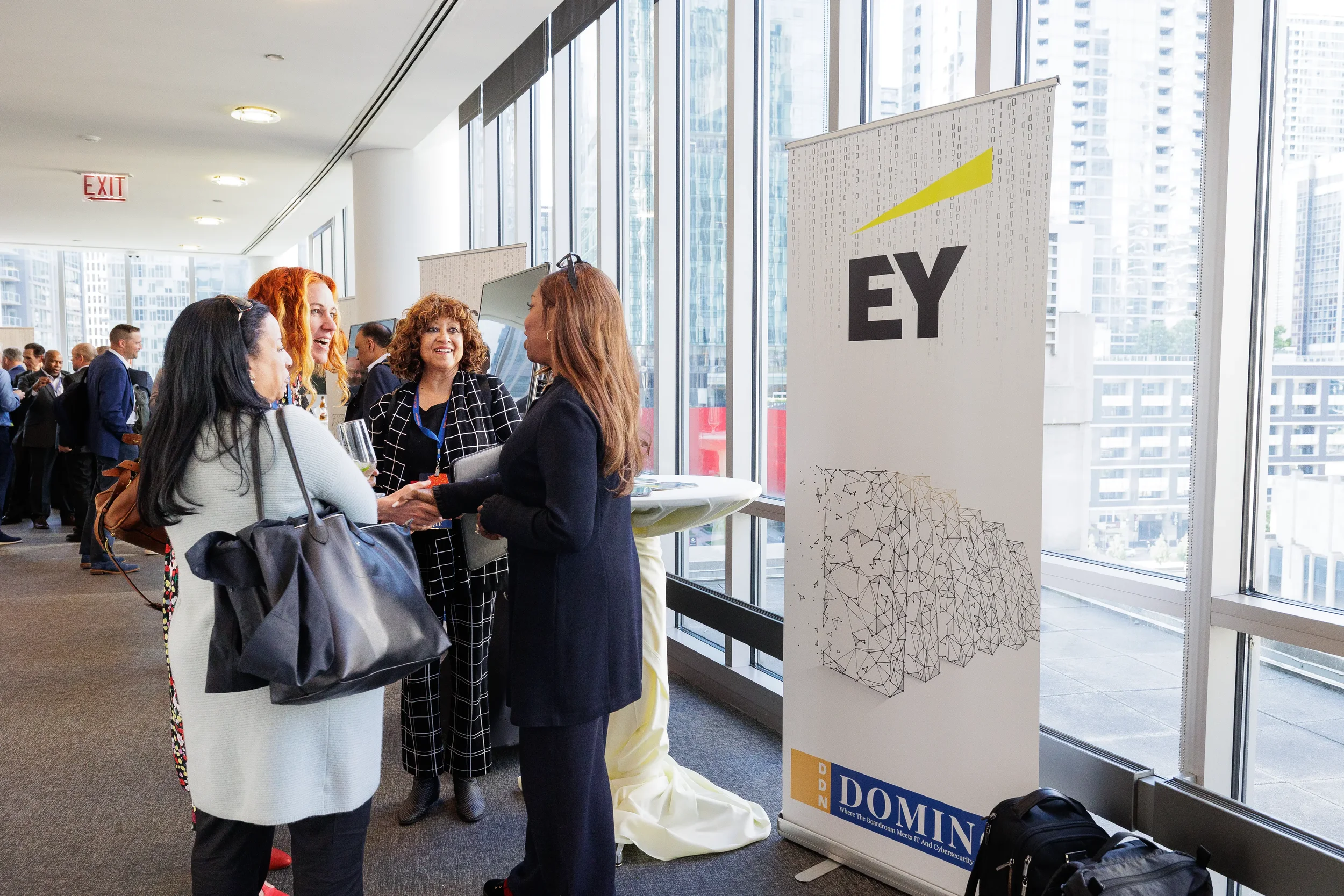 Attendees network and shake hands near sponsor banner with city views at Chicago industry conference