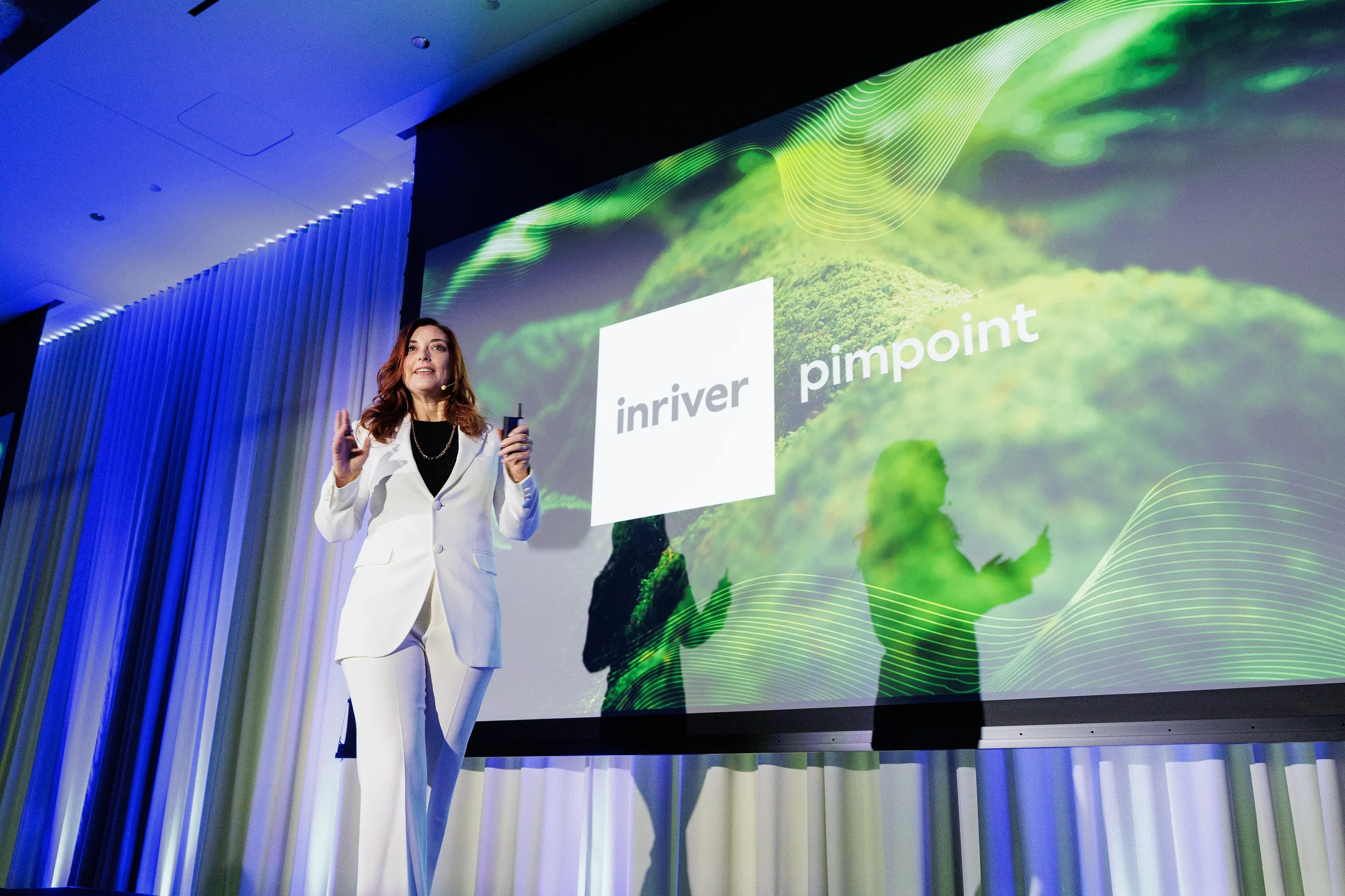 Speaker in white suit gestures on stage in front of projection screen at Orlando industry conference