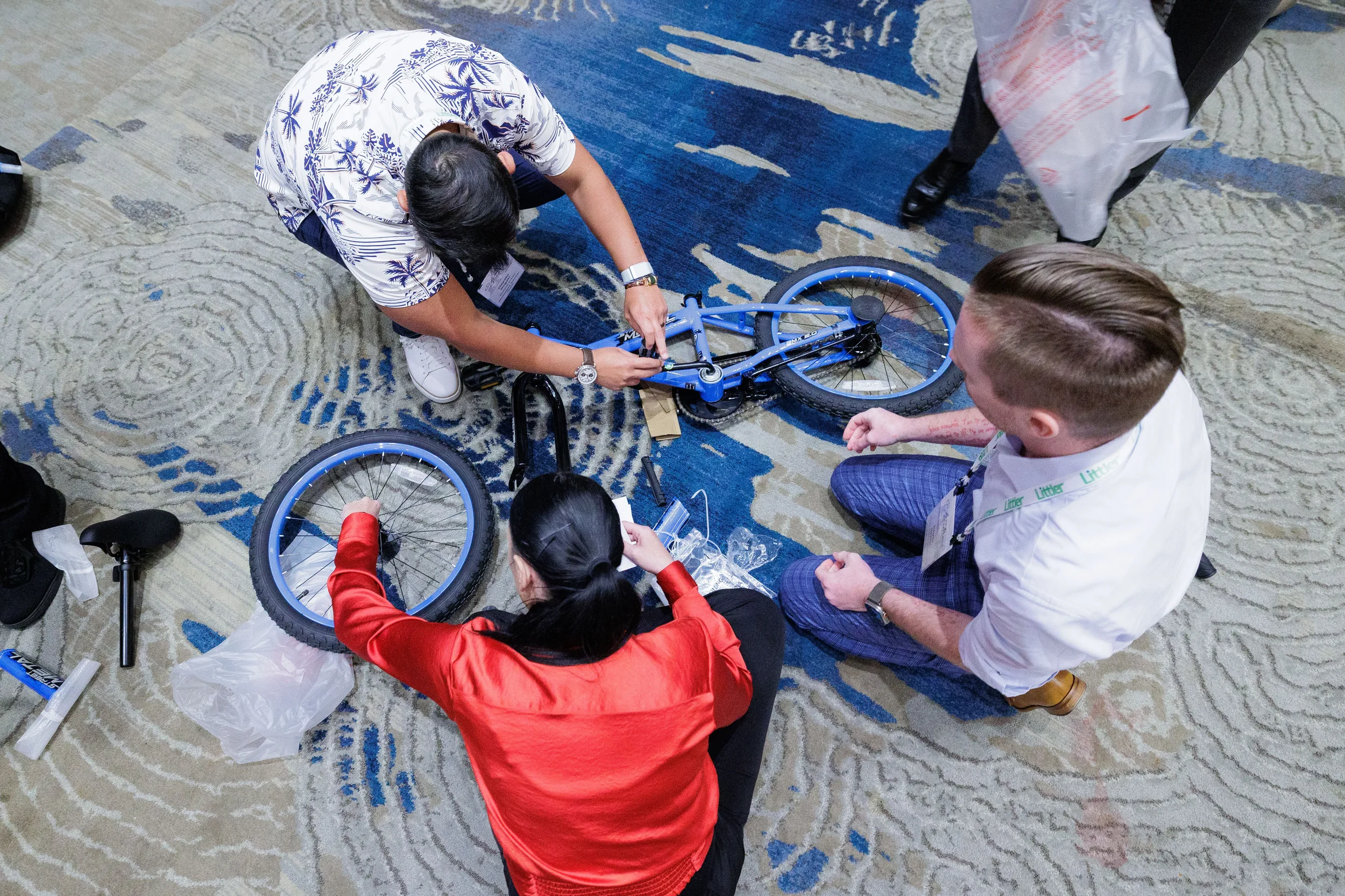 Three attendees with lanyards assemble blue bicycle on floor during Chicago corporate conference team building