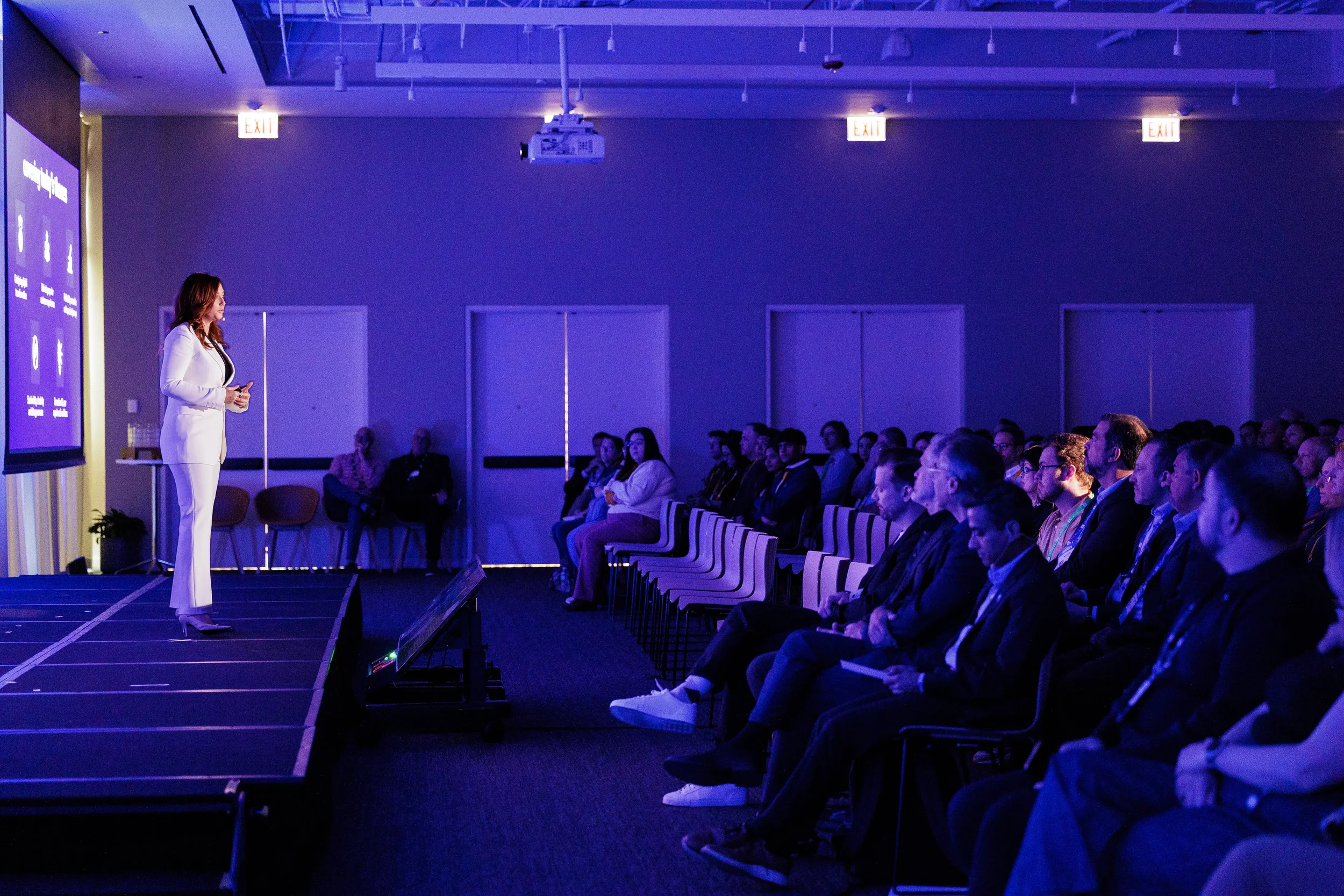 Audience watches speaker on stage in purple-lit room during Orlando industry conference session