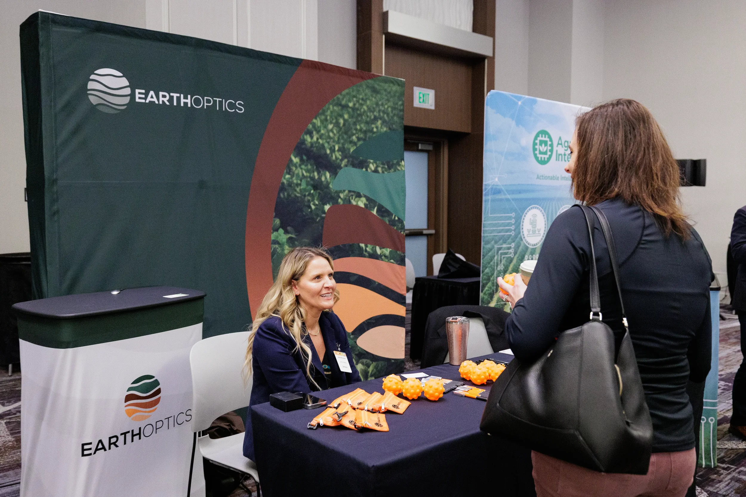 Attendees converse at exhibitor booth displaying products during Orlando trade show event
