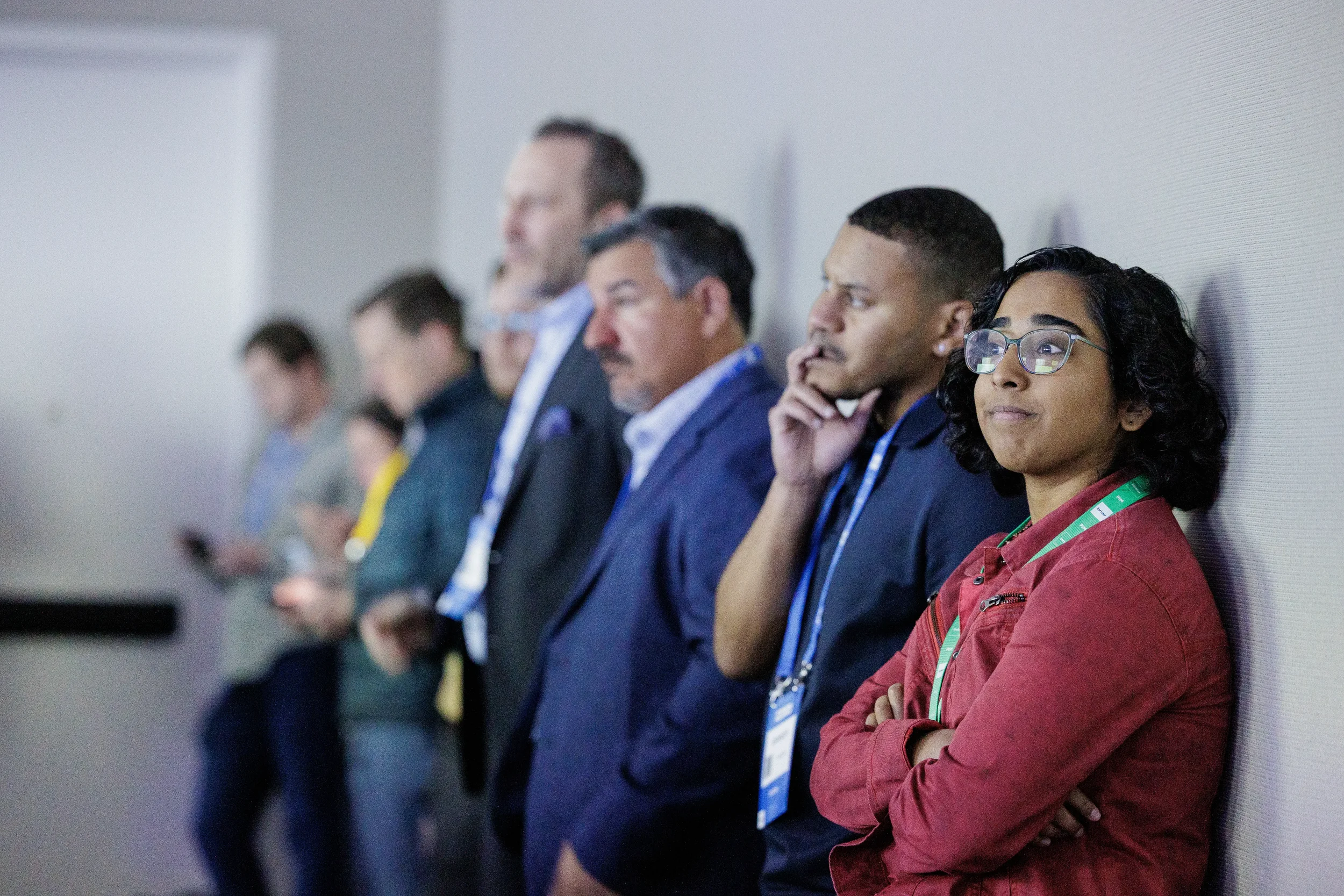 Attendees with lanyards stand along wall watching session at Chicago corporate conference