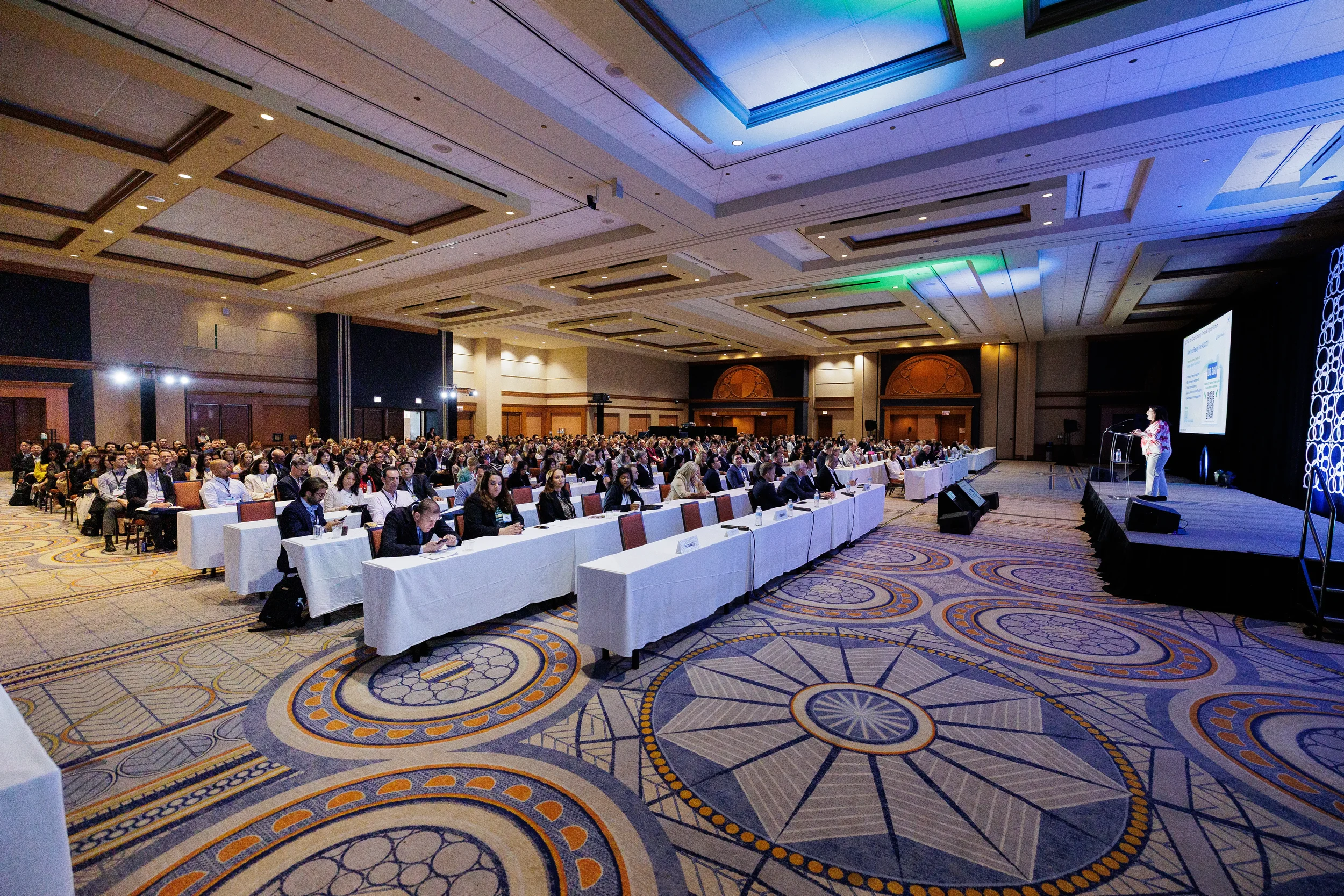 Wide view of packed ballroom audience at long tables watching presenter at Orlando industry conference
