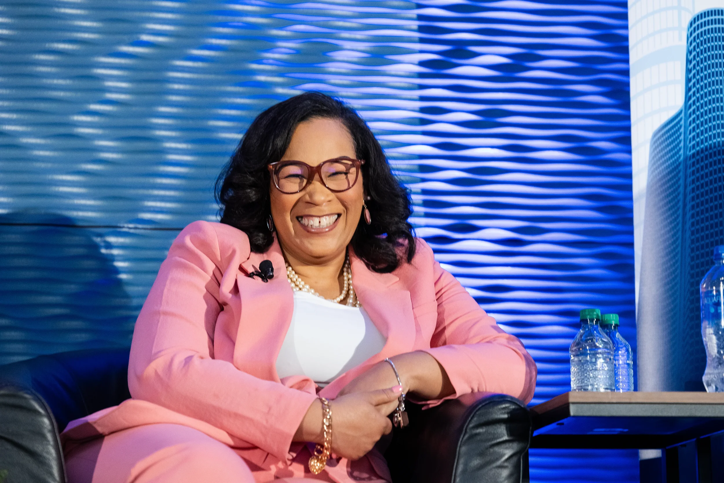 Speaker laughs while seated on stage with branded backdrop at Chicago corporate conference