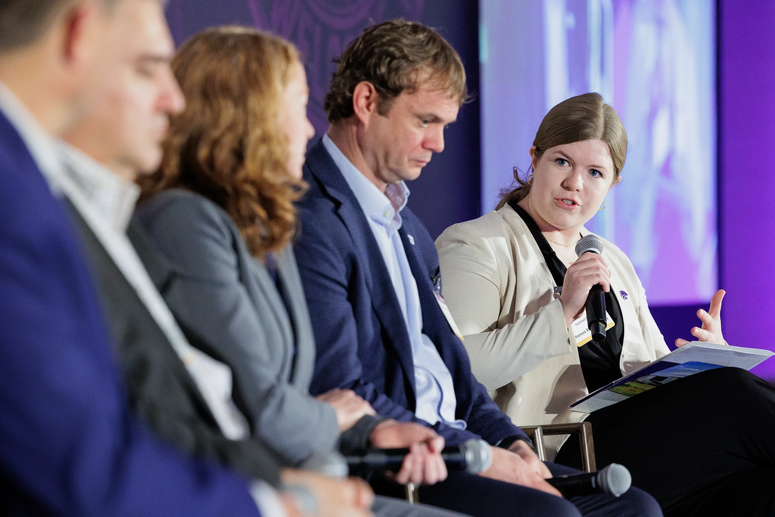 Panelist speaks into microphone while three colleagues listen during Orlando conference panel discussion