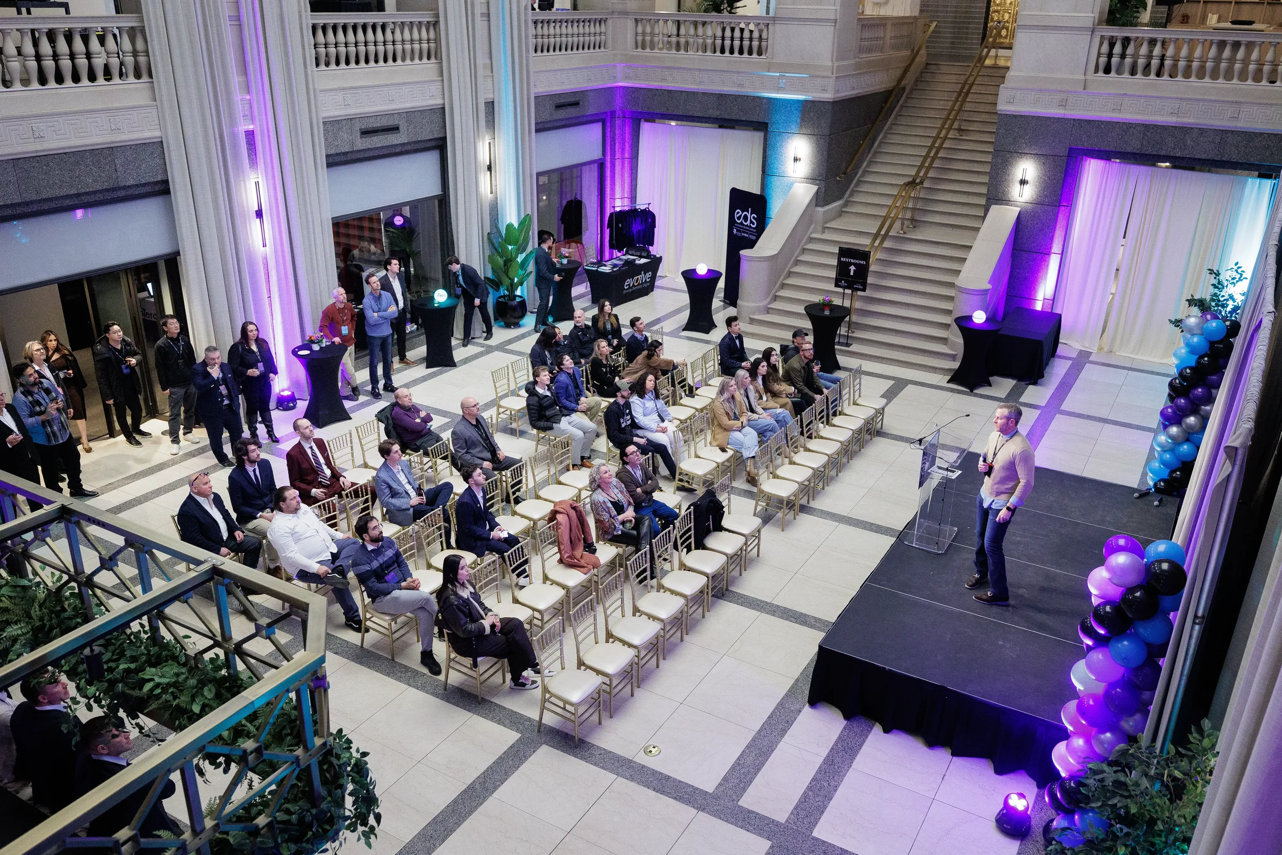 Overhead view of attendees seated in grand ballroom as speaker presents on stage at Orlando event