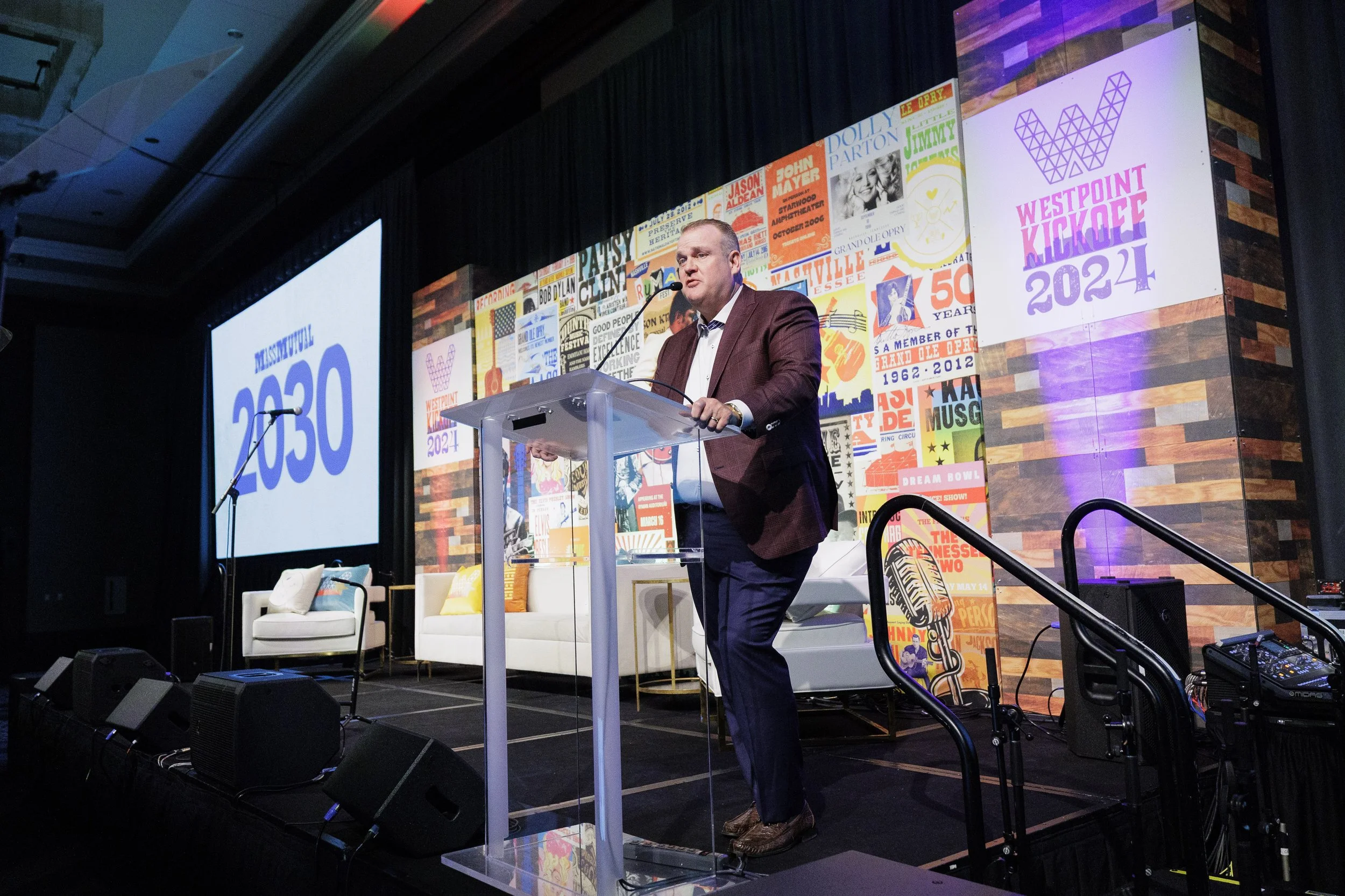 Executive presenting at clear podium on colorfully branded stage at corporate sales kickoff event in Orlando