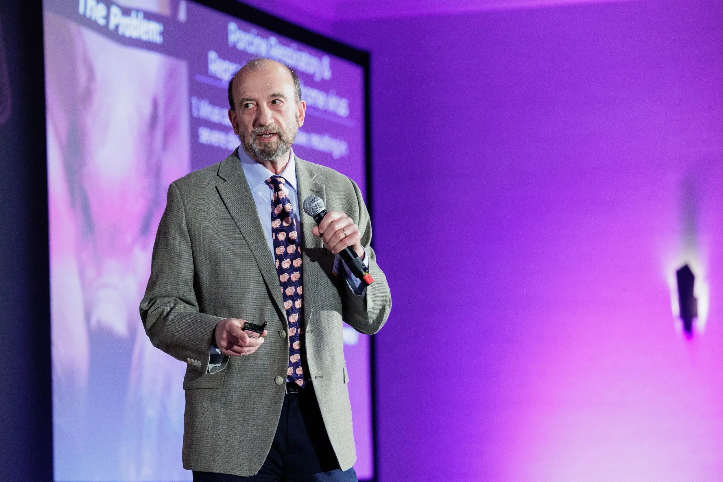 Speaker presents with microphone on stage with purple lighting at Orlando industry summit