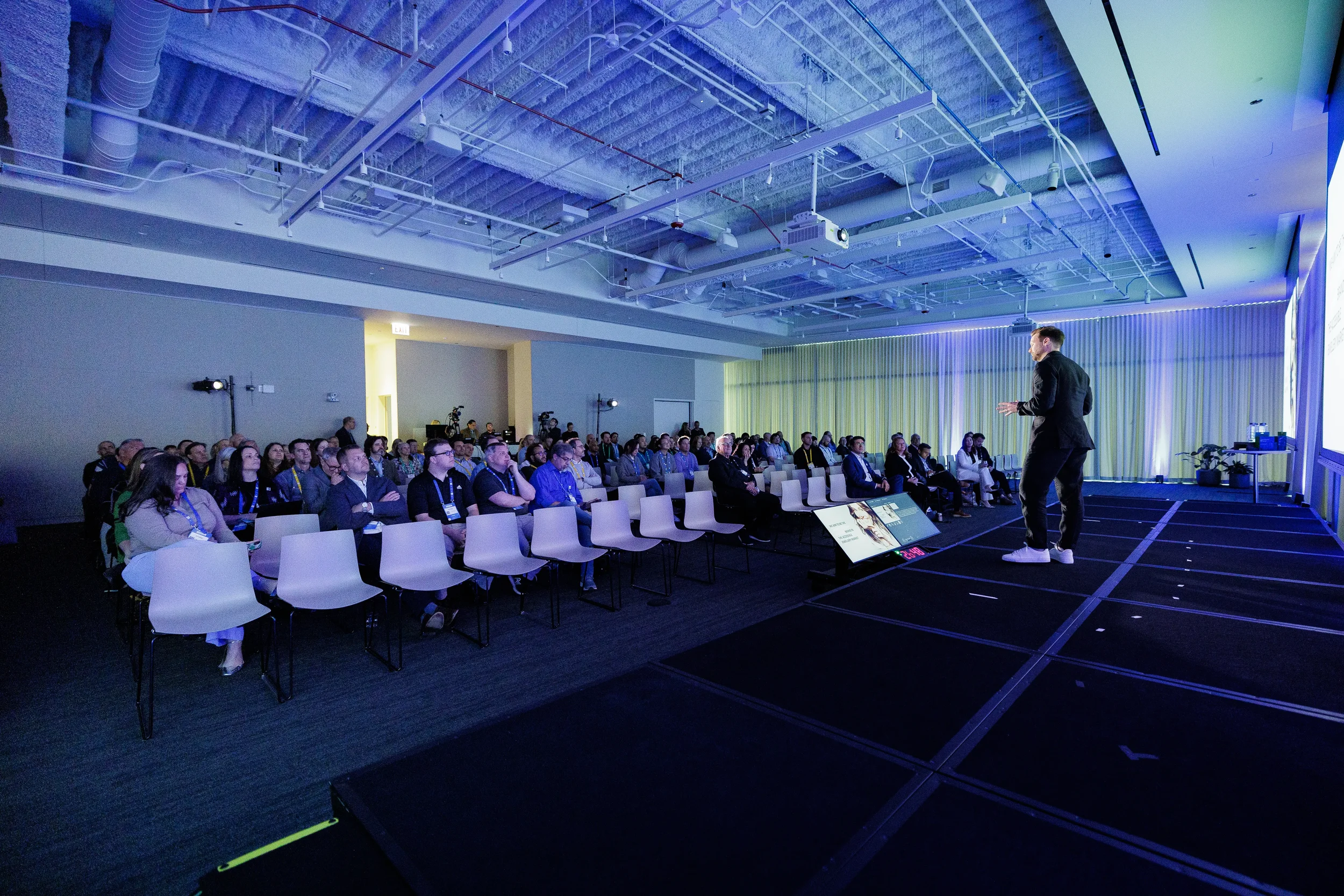 Speaker presents to seated audience in blue-lit ballroom at Chicago industry conference