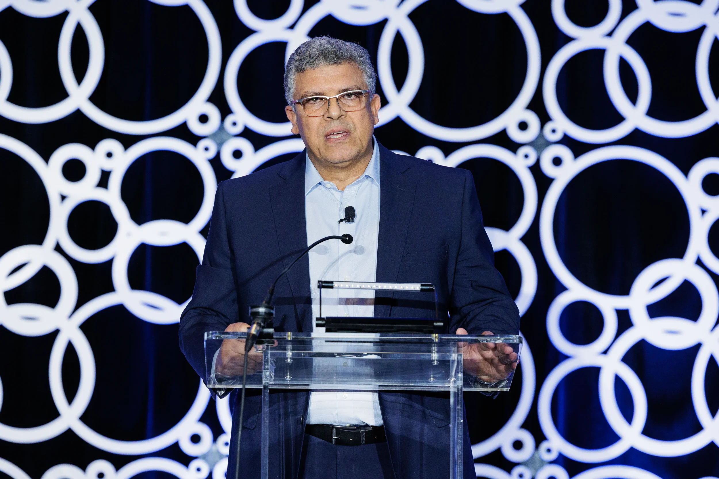 Speaker presents from podium with illuminated circular backdrop at Chicago industry conference