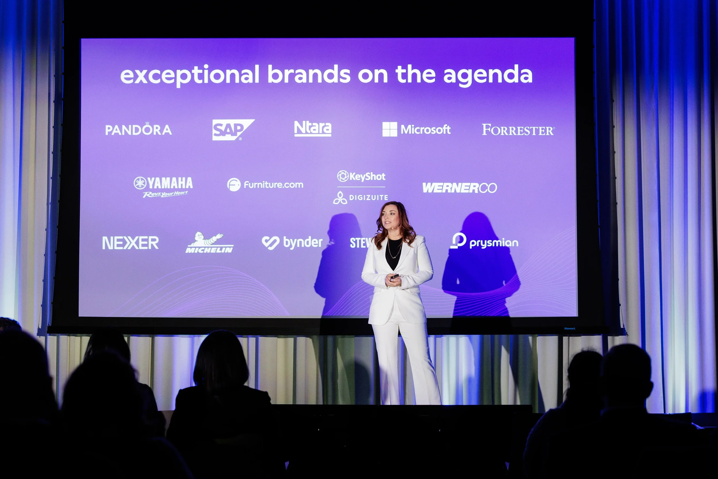 Speaker in white suit presents on stage before large projection screen at Orlando corporate conference