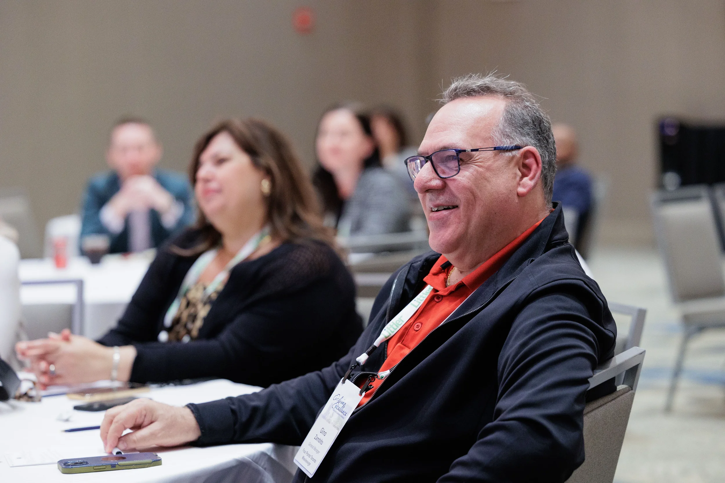 Attendees with lanyards smile while seated at round tables during Orlando corporate conference session