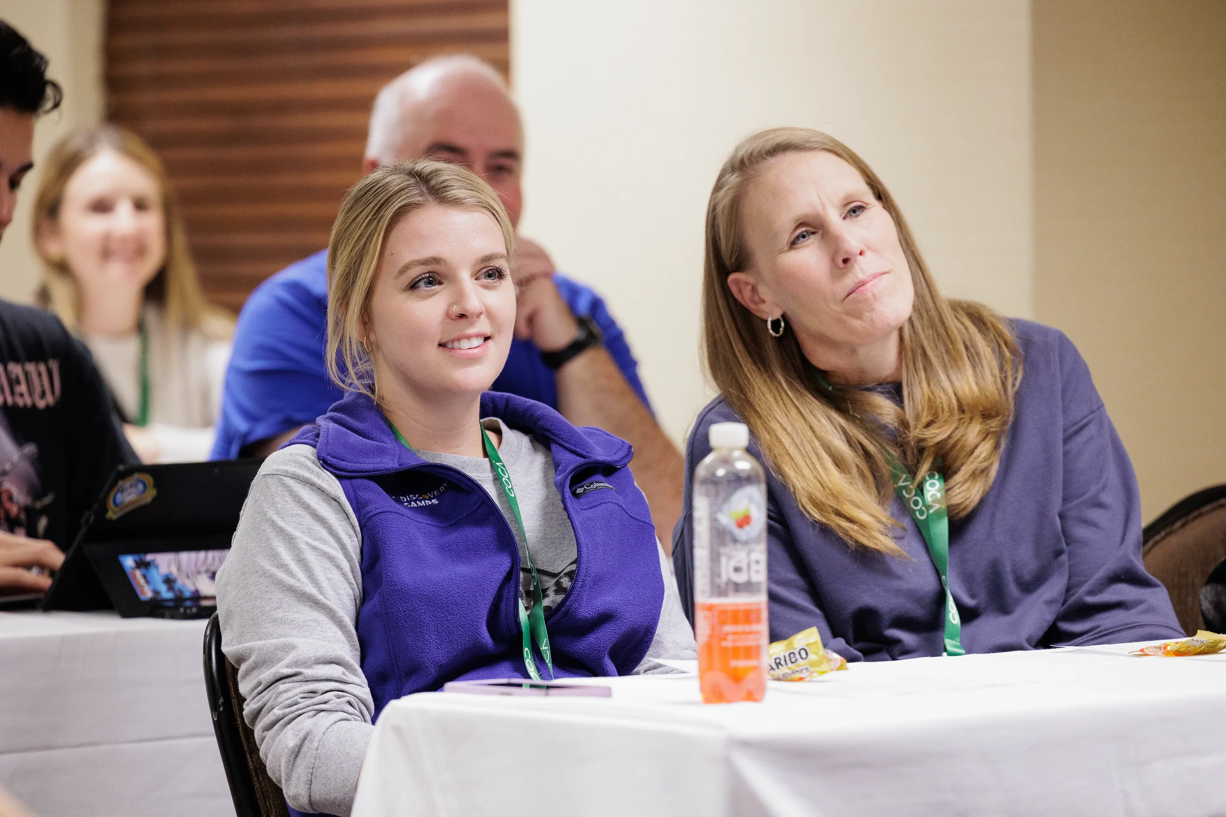 Two attendees wearing conference lanyards watch breakout session from table at Orlando nonprofit conference event