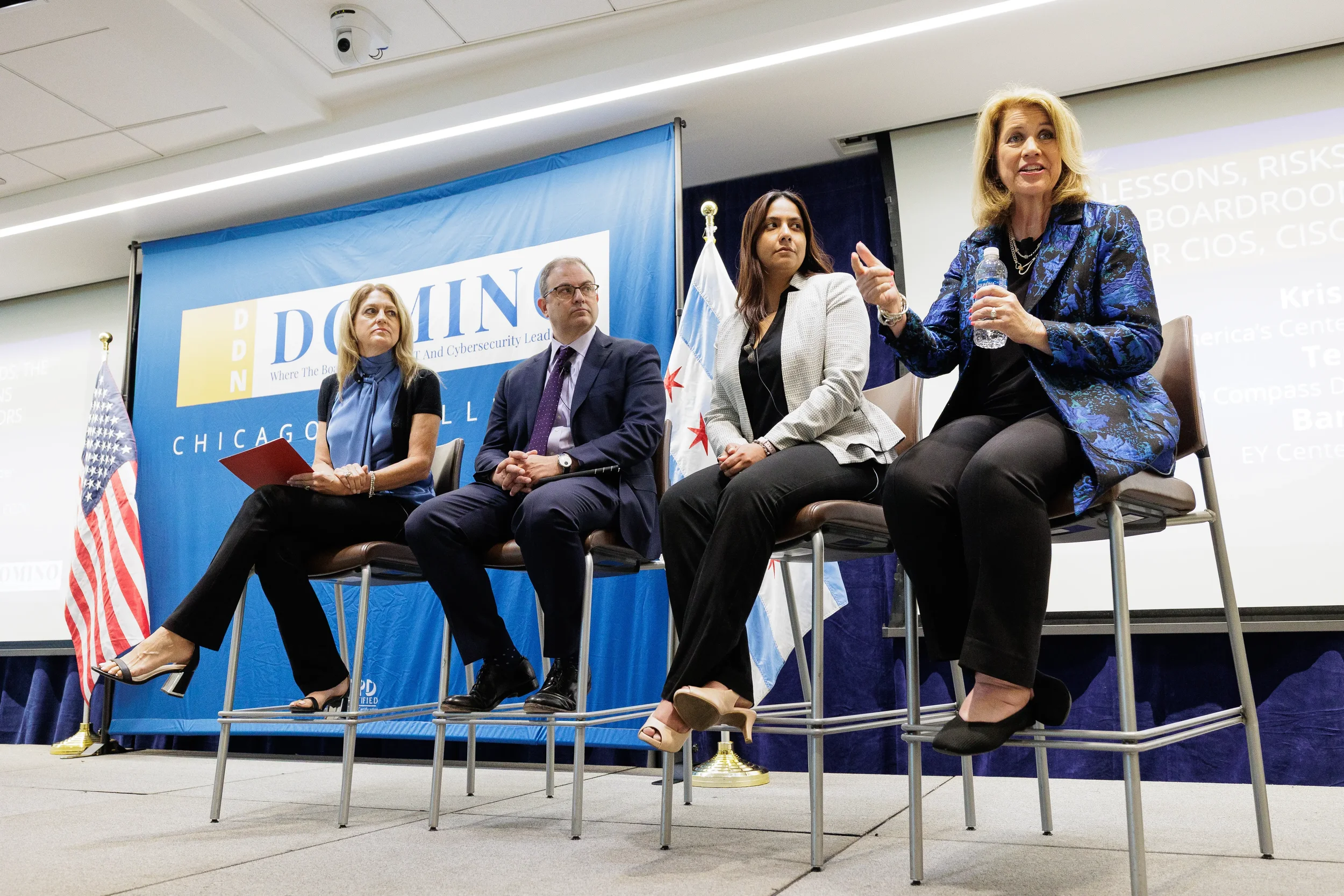 Four panelists seated on stools in front of branded backdrop and flags at Orlando corporate conference