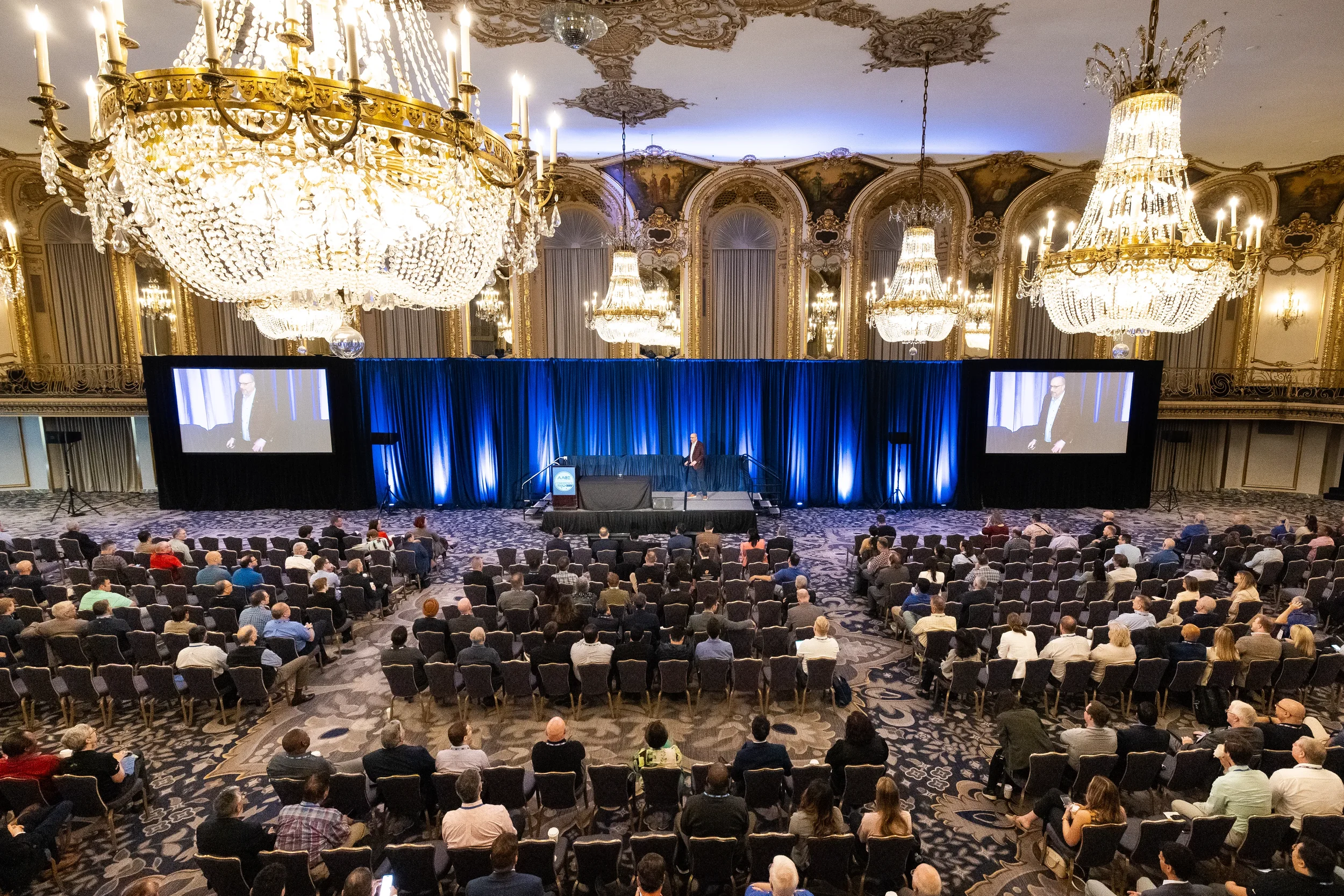 Wide view of ornate ballroom with chandeliers during Orlando conference keynote presentation