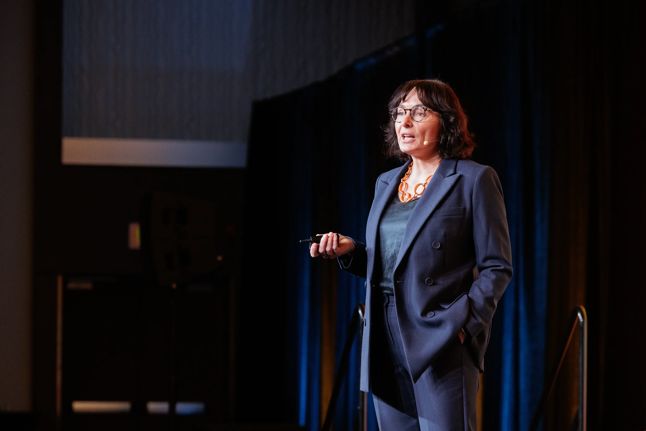 Female keynote speaker in navy suit with earpiece presents on stage at Orlando corporate industry conference