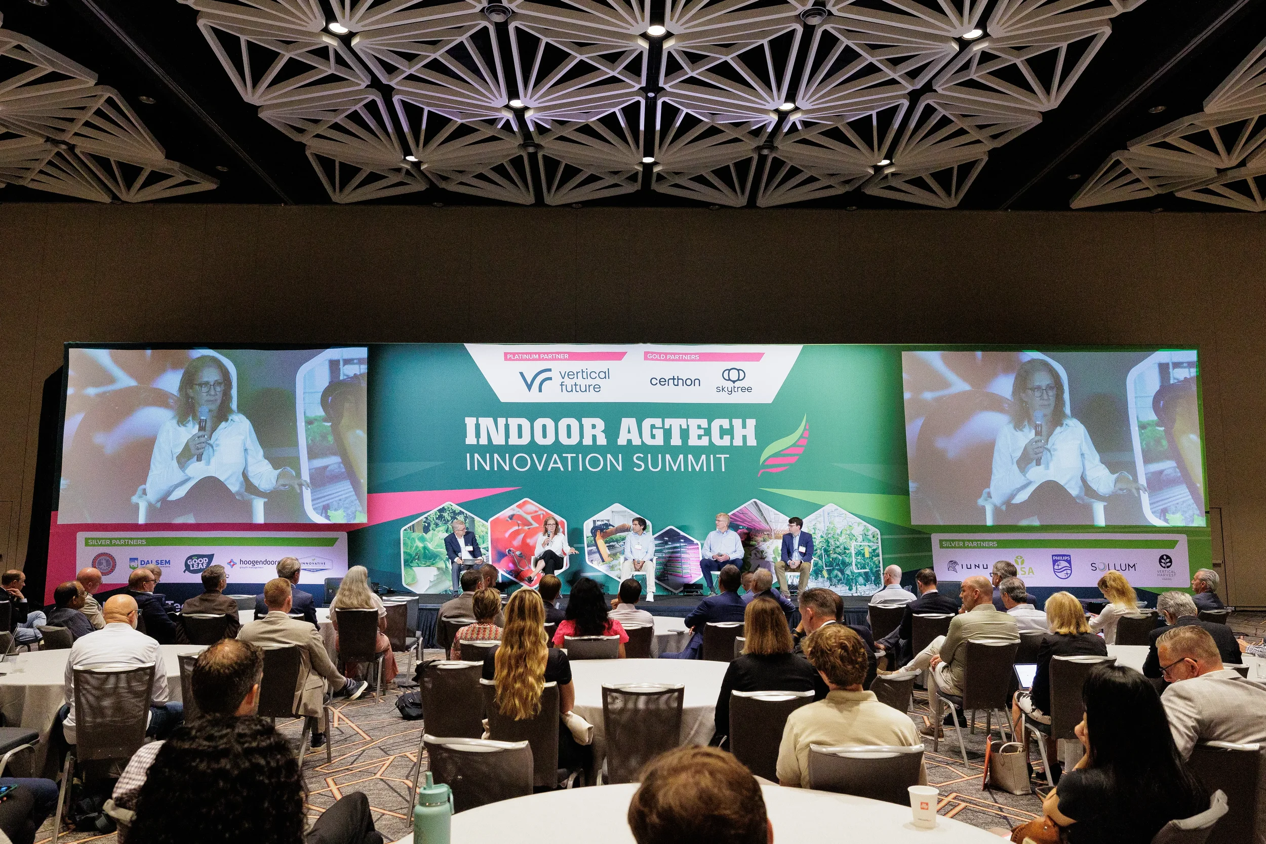 Wide view of panel discussion on stage with audience seated at round tables at Orlando conference