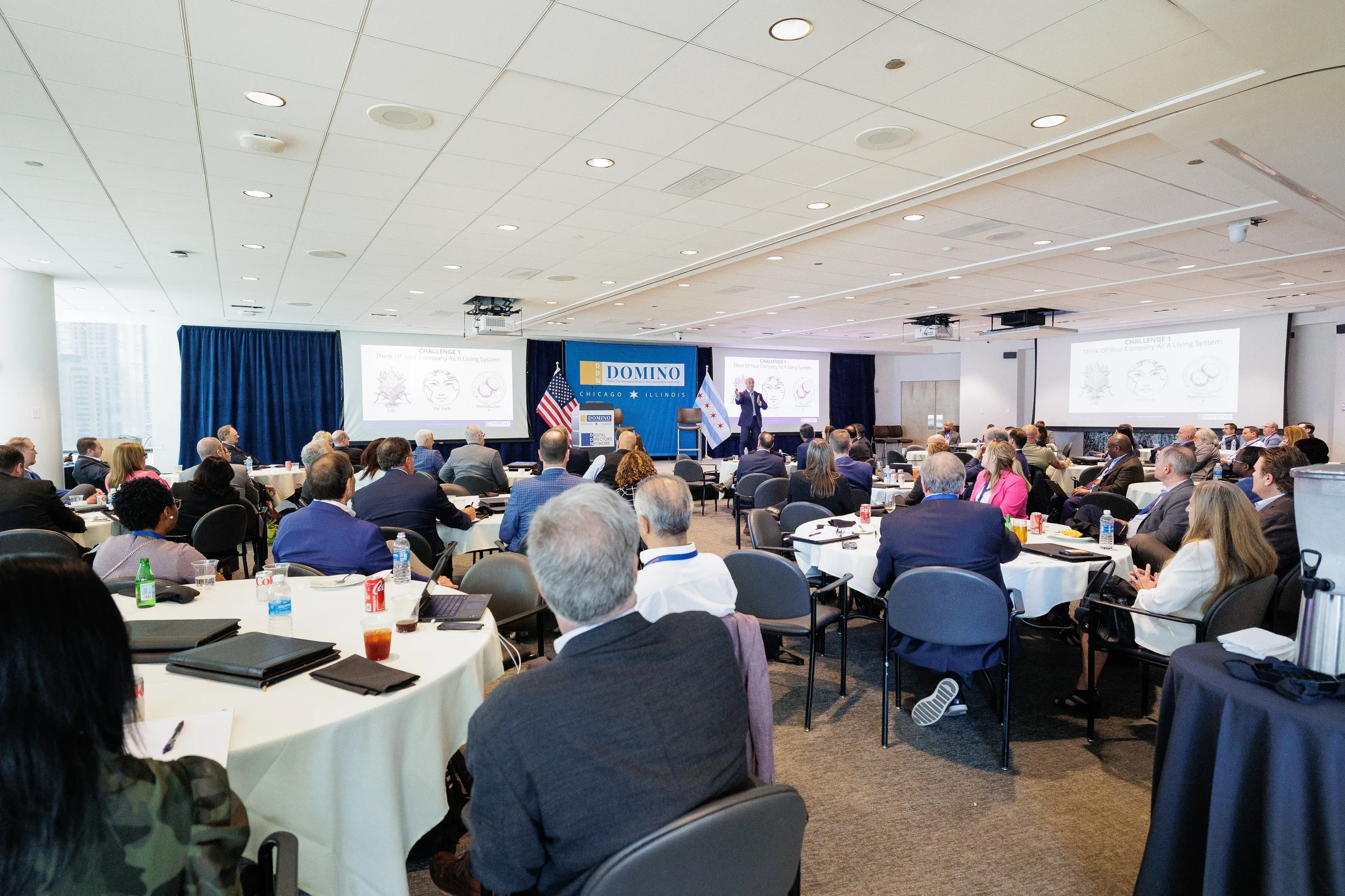 Speaker presents on branded stage to full room of attendees at round tables during Orlando industry conference