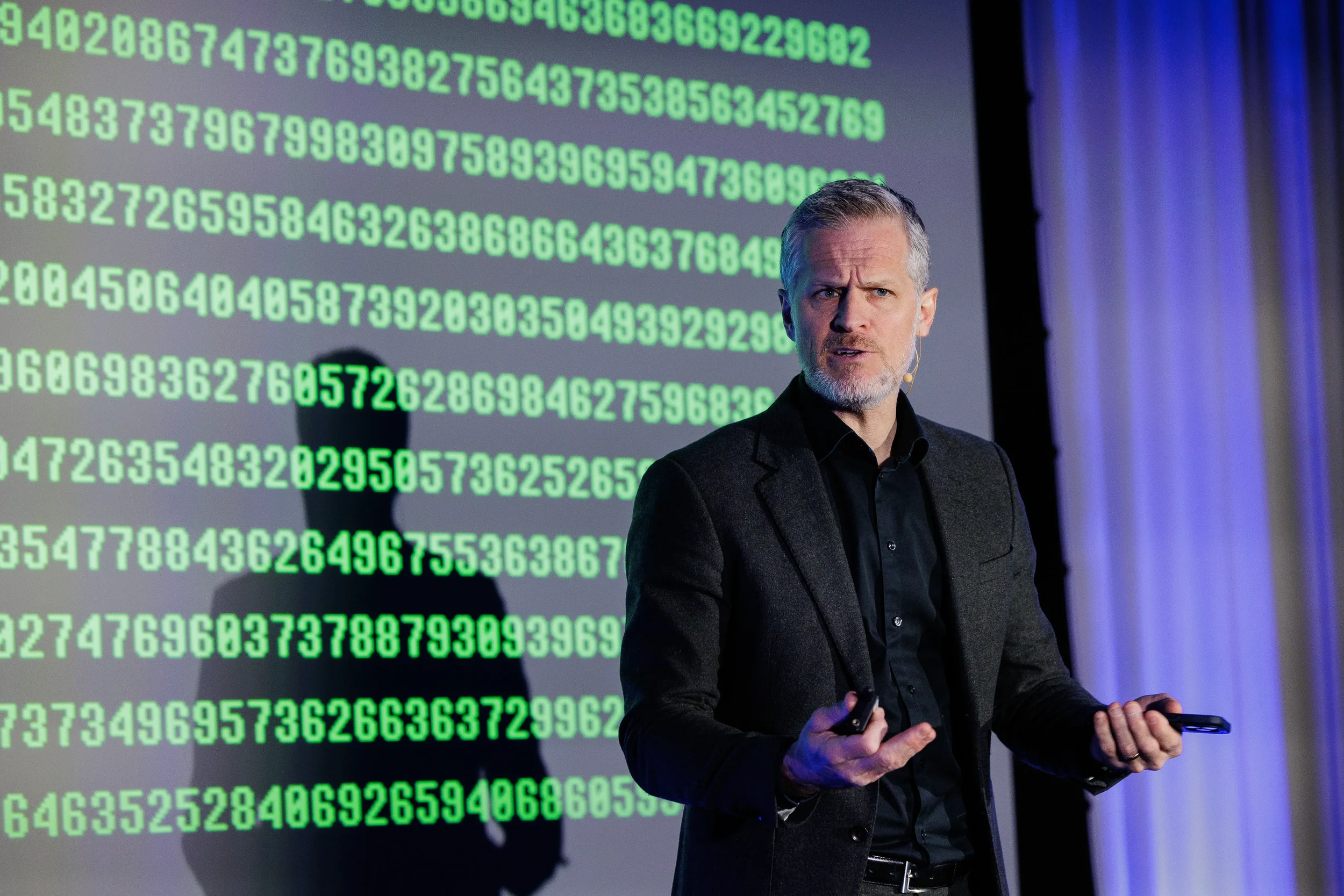 Speaker gestures on stage in front of green digital projection screen at Orlando industry conference