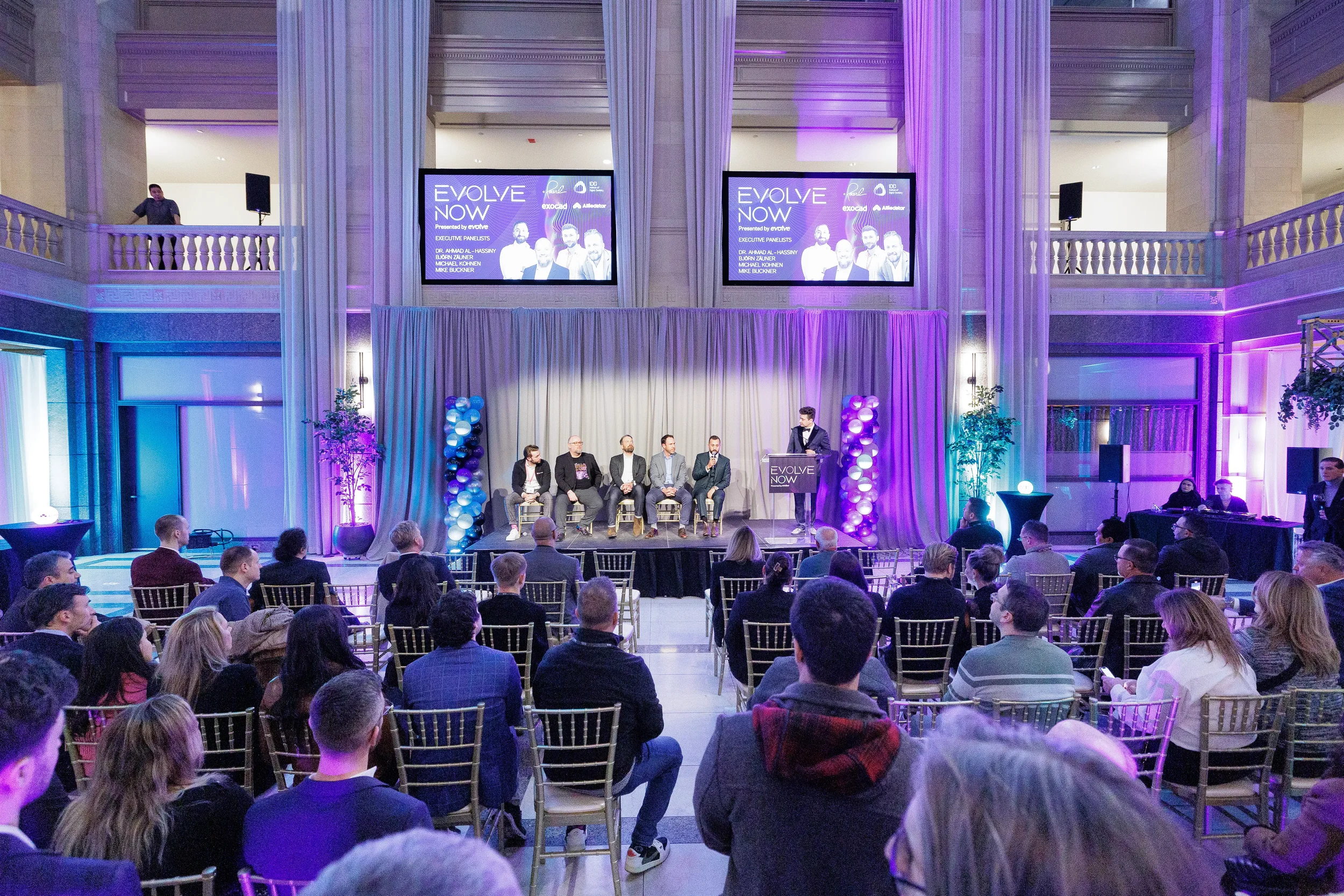 Four panelists seated on stage with moderator address full audience in grand hall at Chicago corporate event