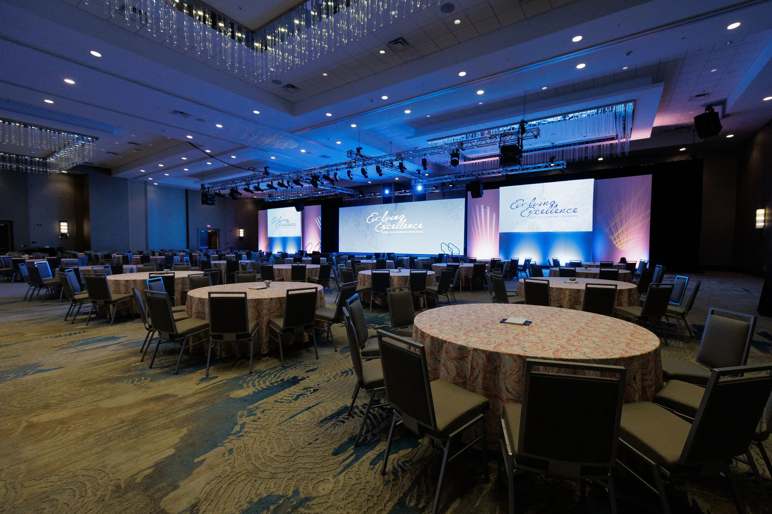 Ballroom with round tables and branded projection screens on blue-lit stage at Chicago corporate event