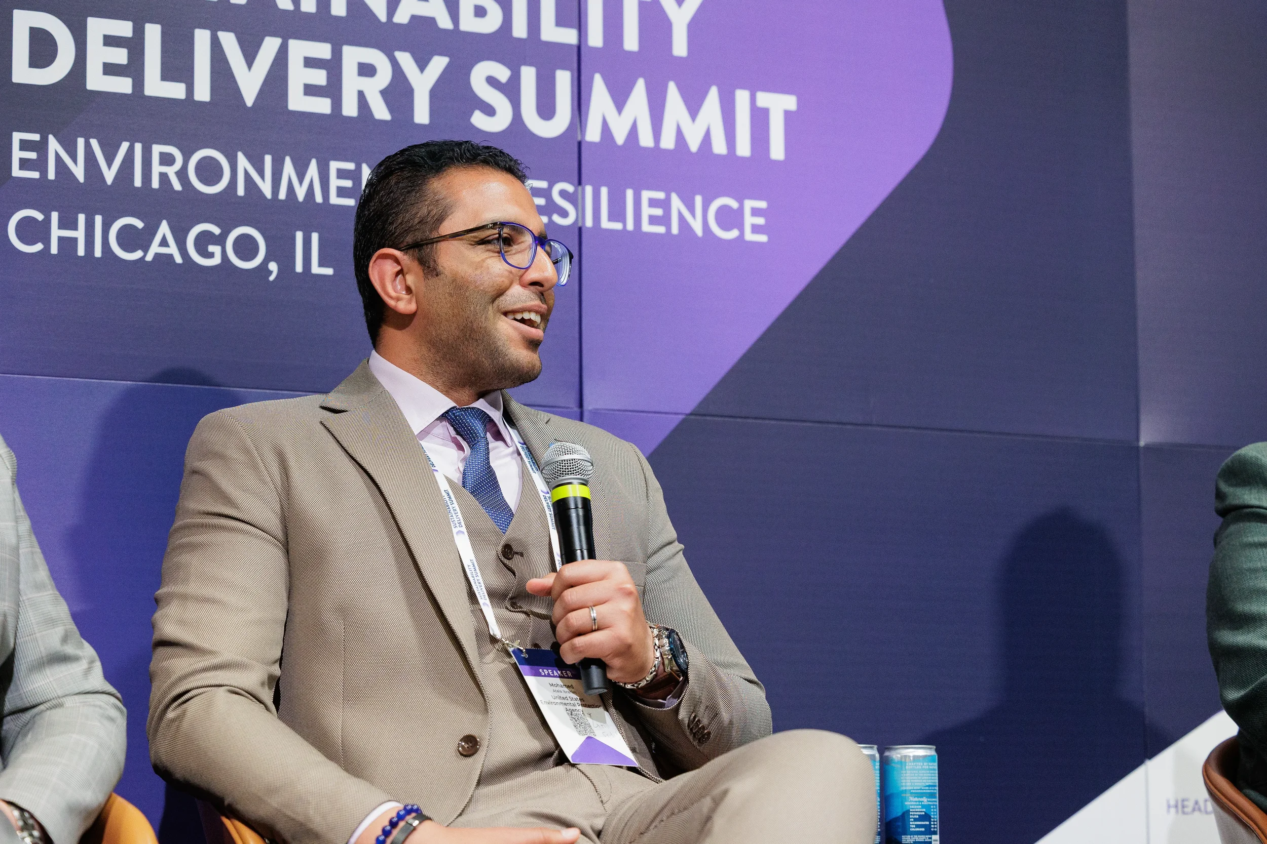 Panelist smiles while speaking into microphone on branded stage at Orlando industry summit