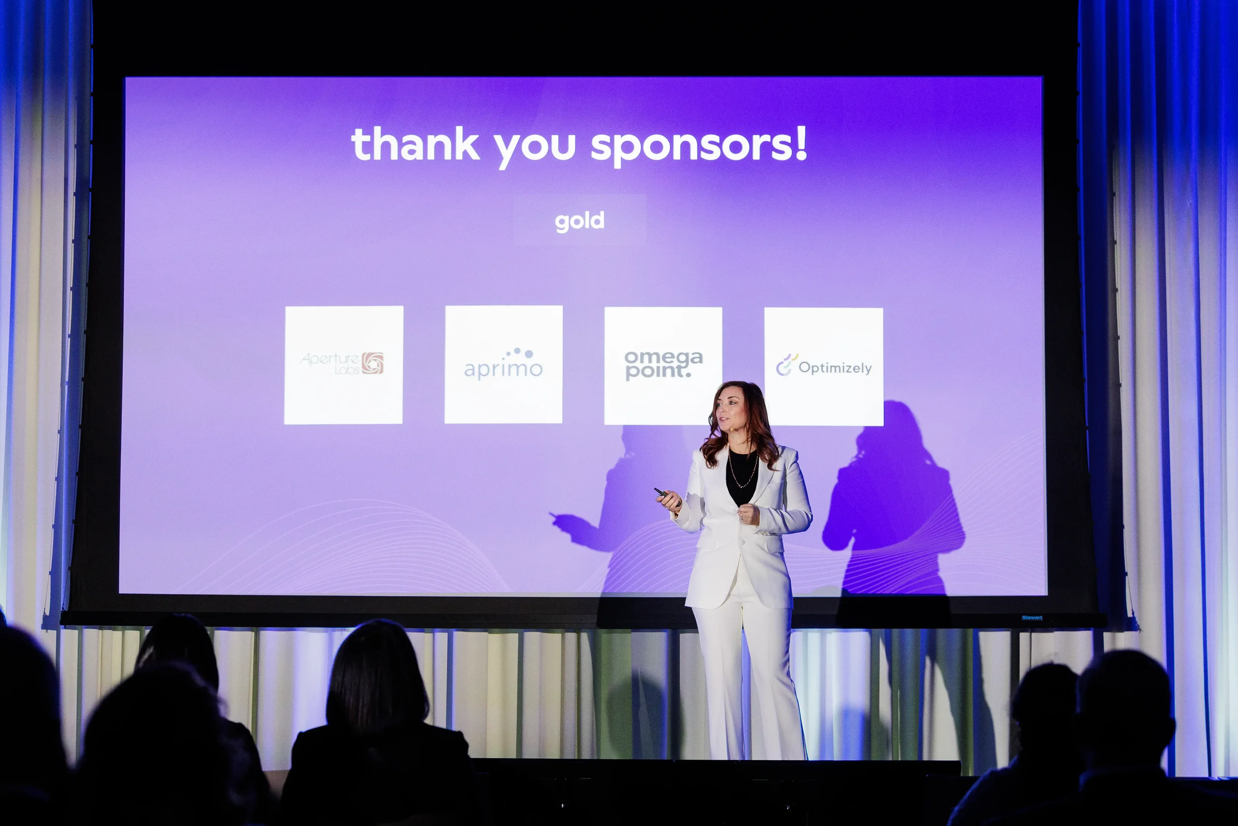 Speaker in white suit presents sponsor slide to audience at Chicago corporate conference
