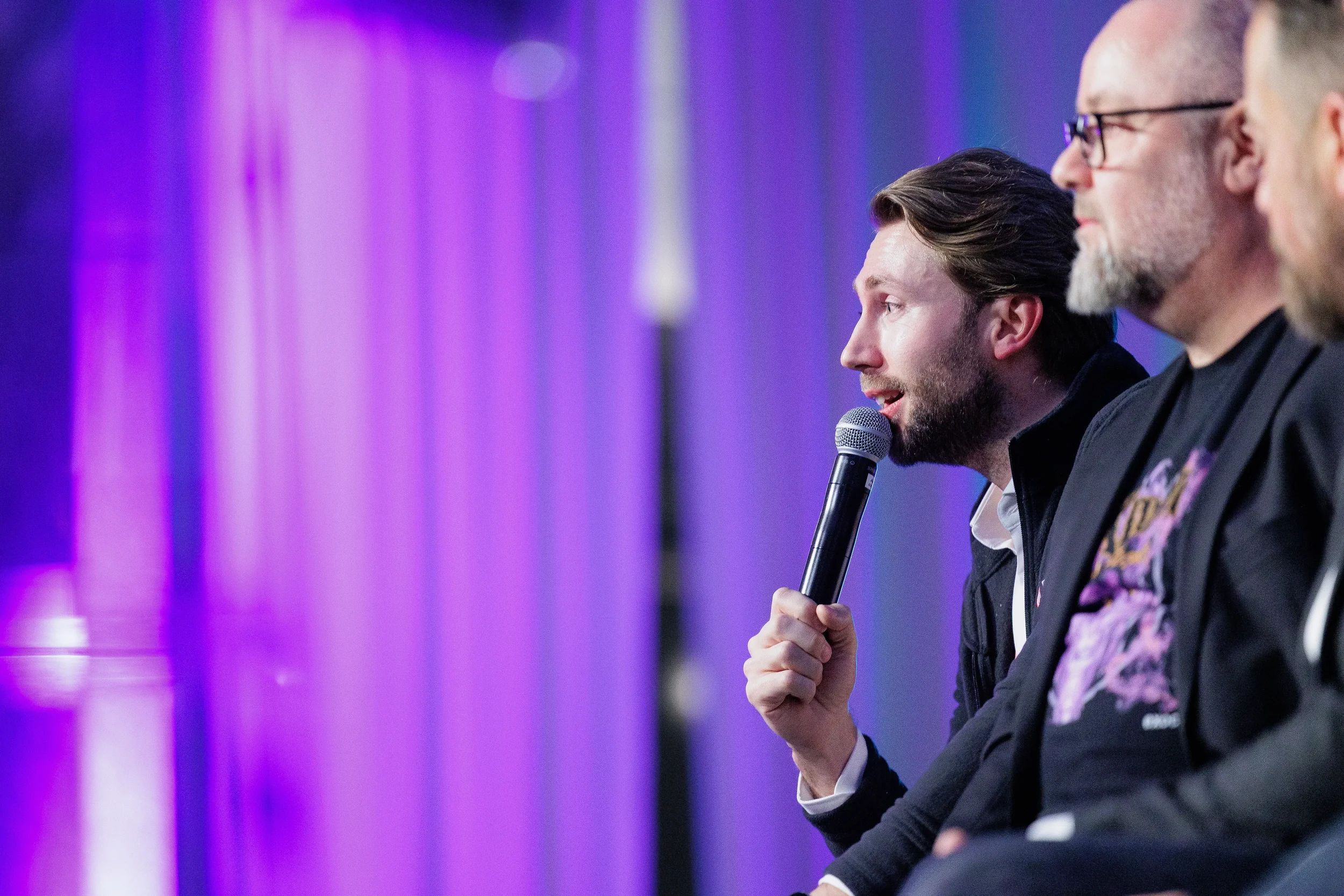 Panelist speaks into microphone in profile view with purple stage lighting at Orlando corporate event