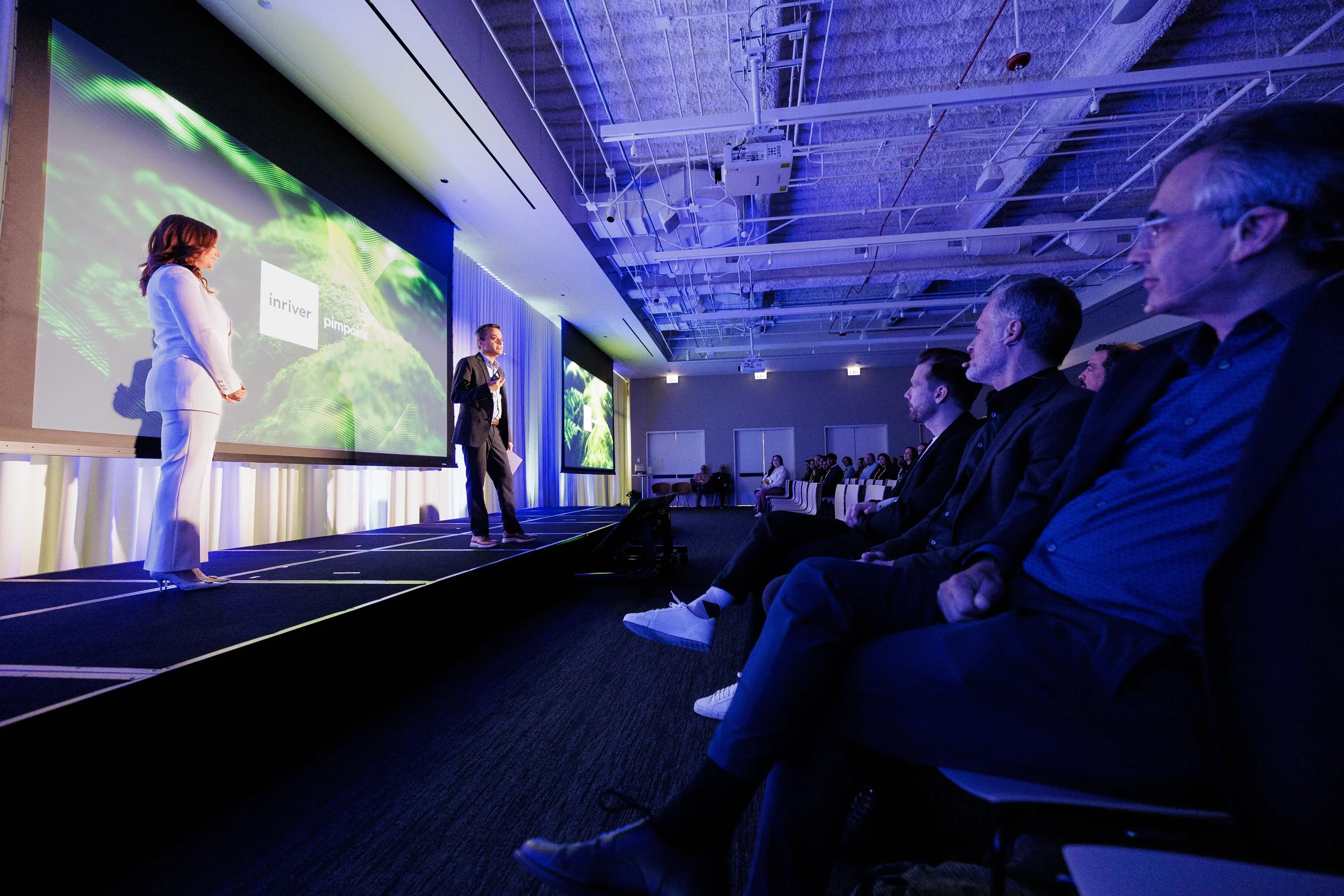 Two speakers on stage in blue lighting with audience in foreground at Orlando industry conference