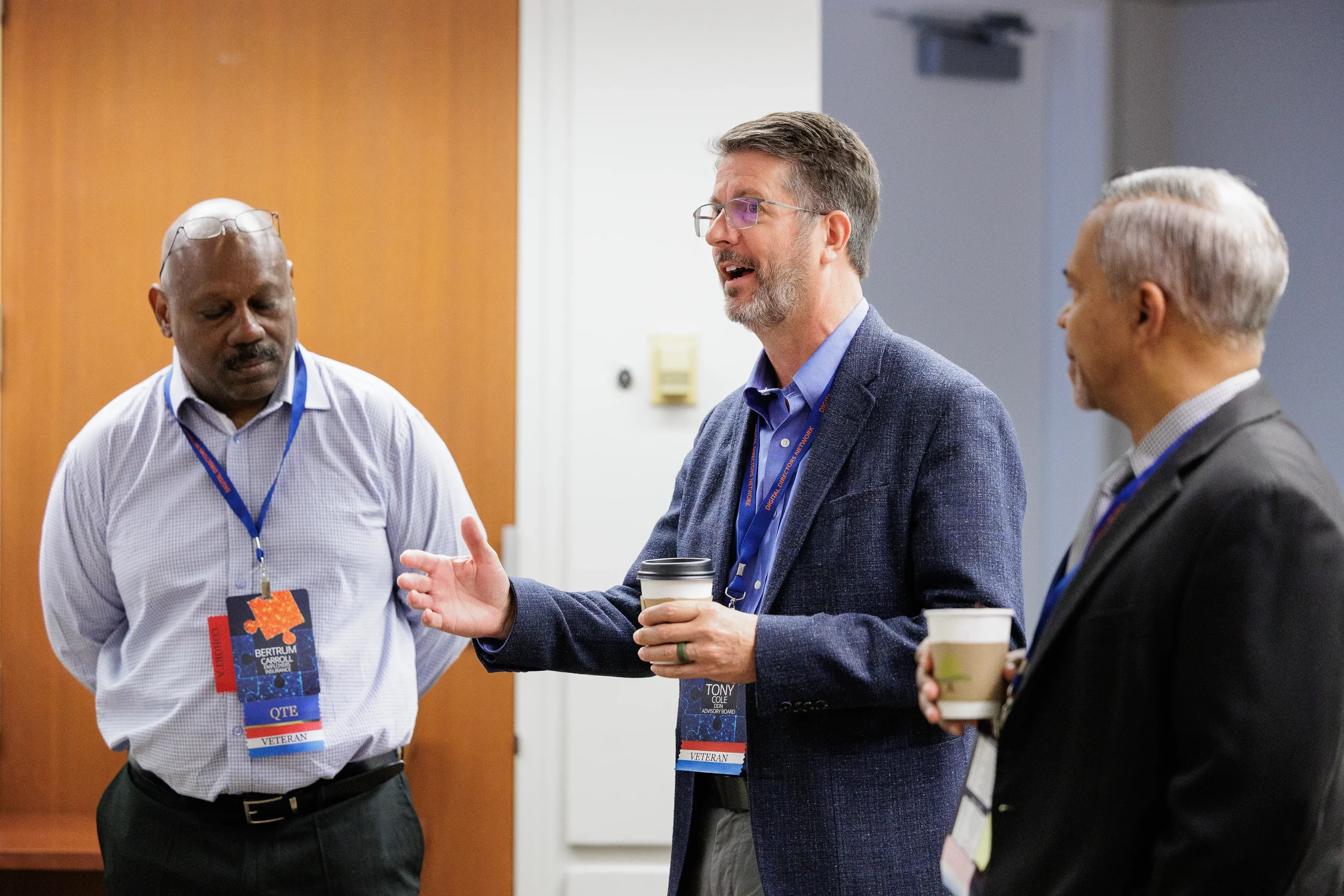 Three attendees with lanyards chat over coffee during networking break at Chicago industry conference