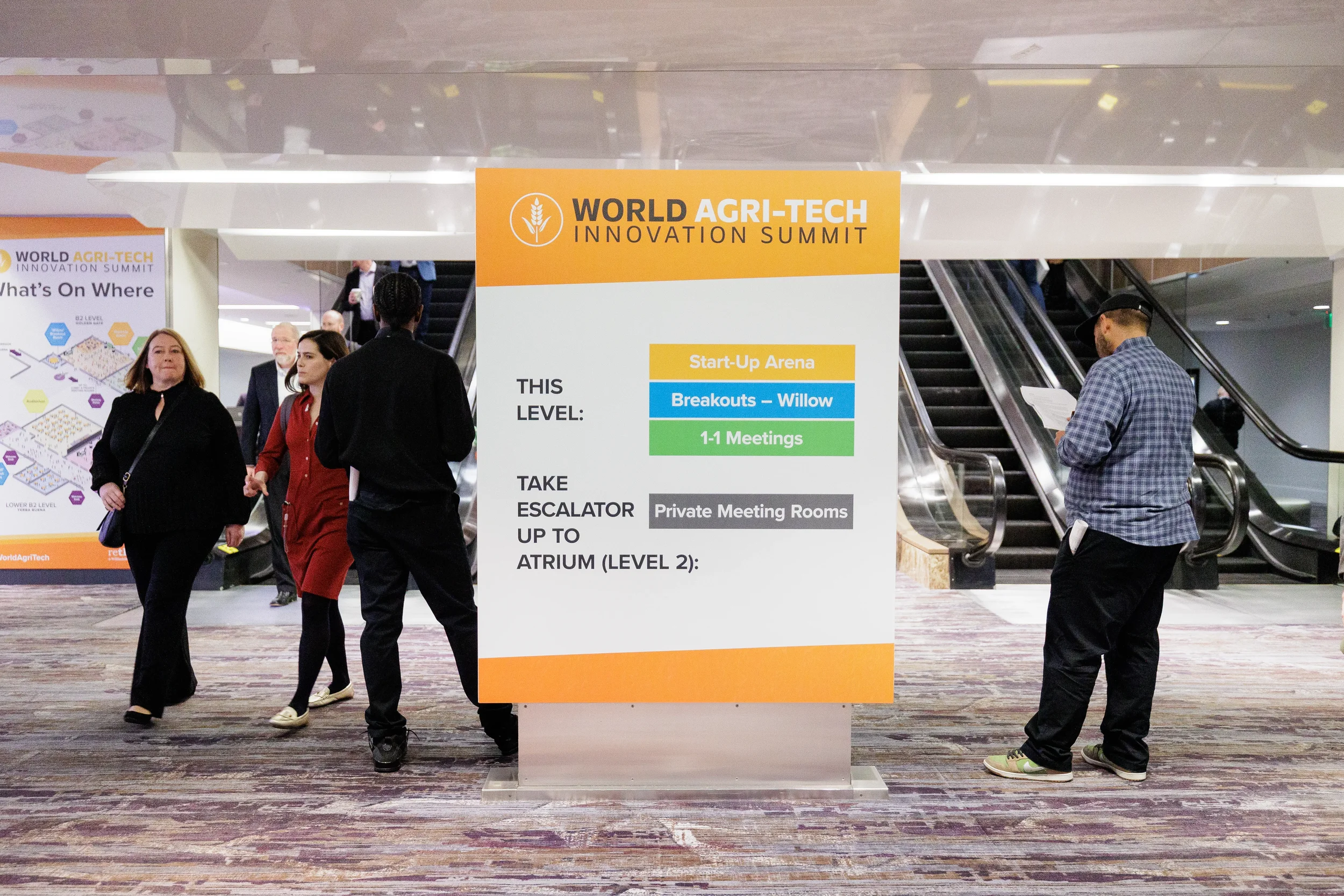 Attendees pass branded wayfinding sign near escalators in Orlando corporate conference venue lobby